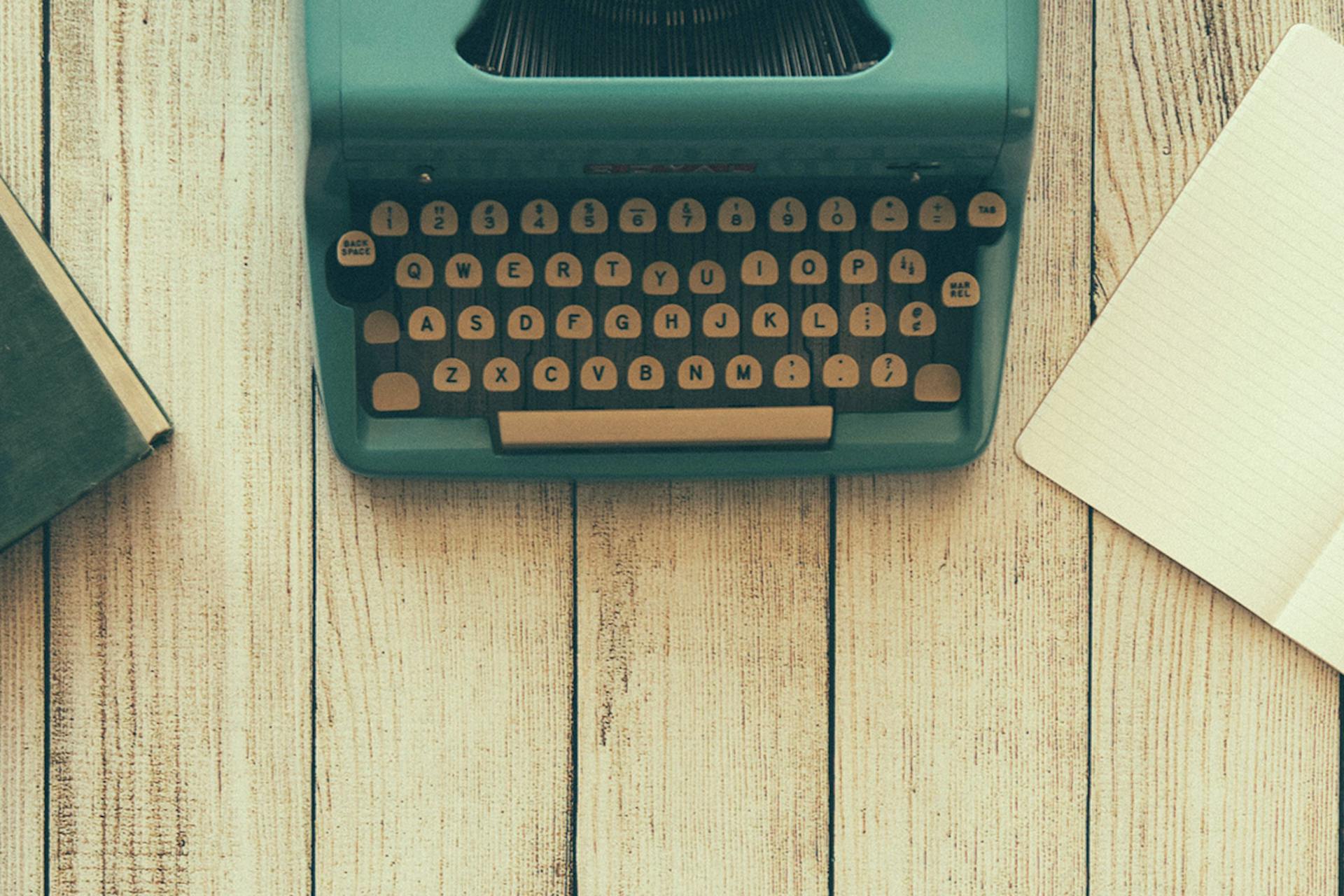 Een foto van een ouderwetse typemachine met een lees notitieboek ernaast op een houten tafel