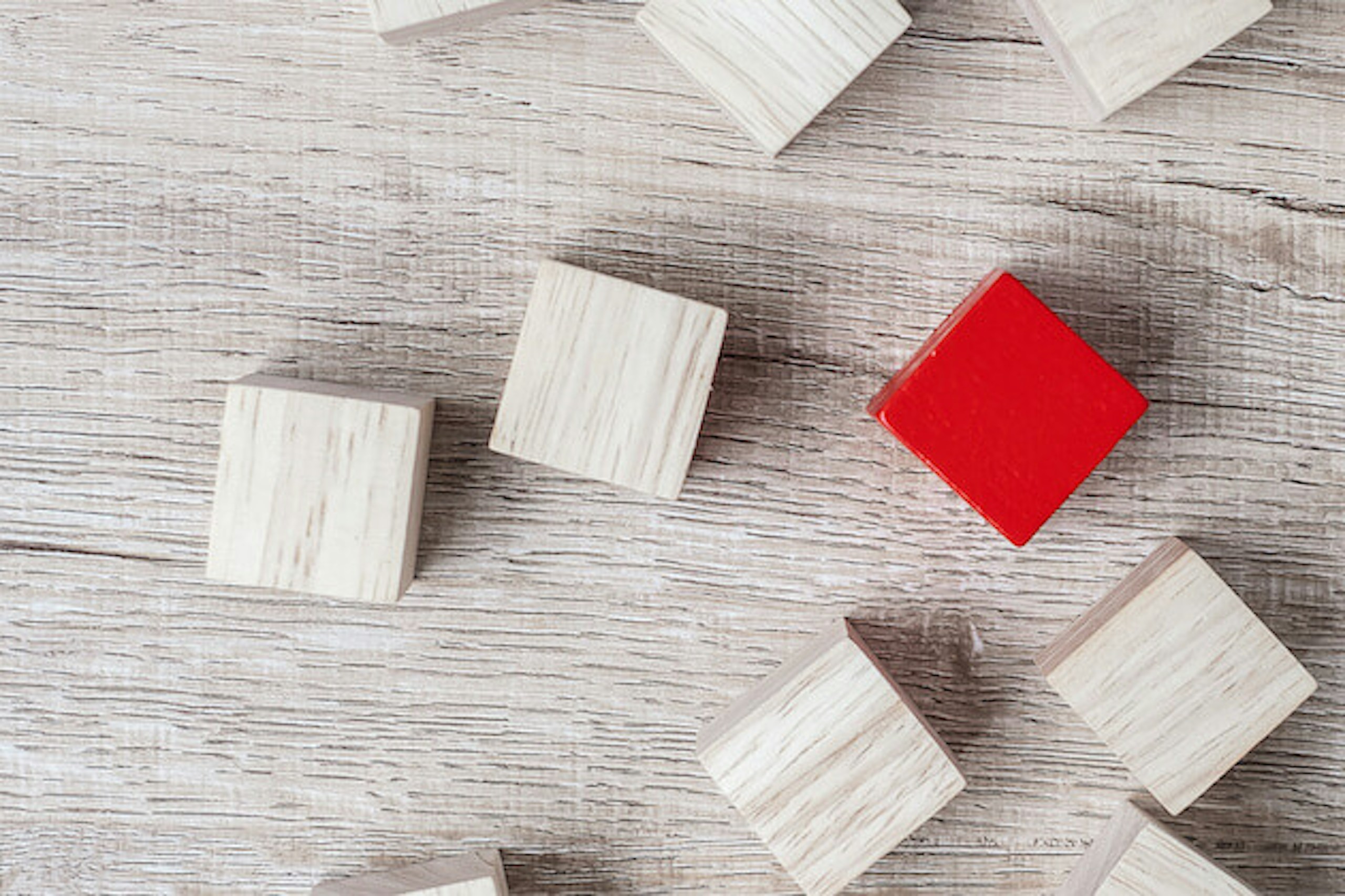 Man sieht einen weiß gestrichenen Holztisch, auf dem viele weiße Holzwürfel zu sehen sind. In der Mitte sticht ein roter Würfel hervor. Dieses Bild ist das Titelbild unseres Beitrags zur Erarbeitung eines USPs / Alleinstellungsmerkmals.