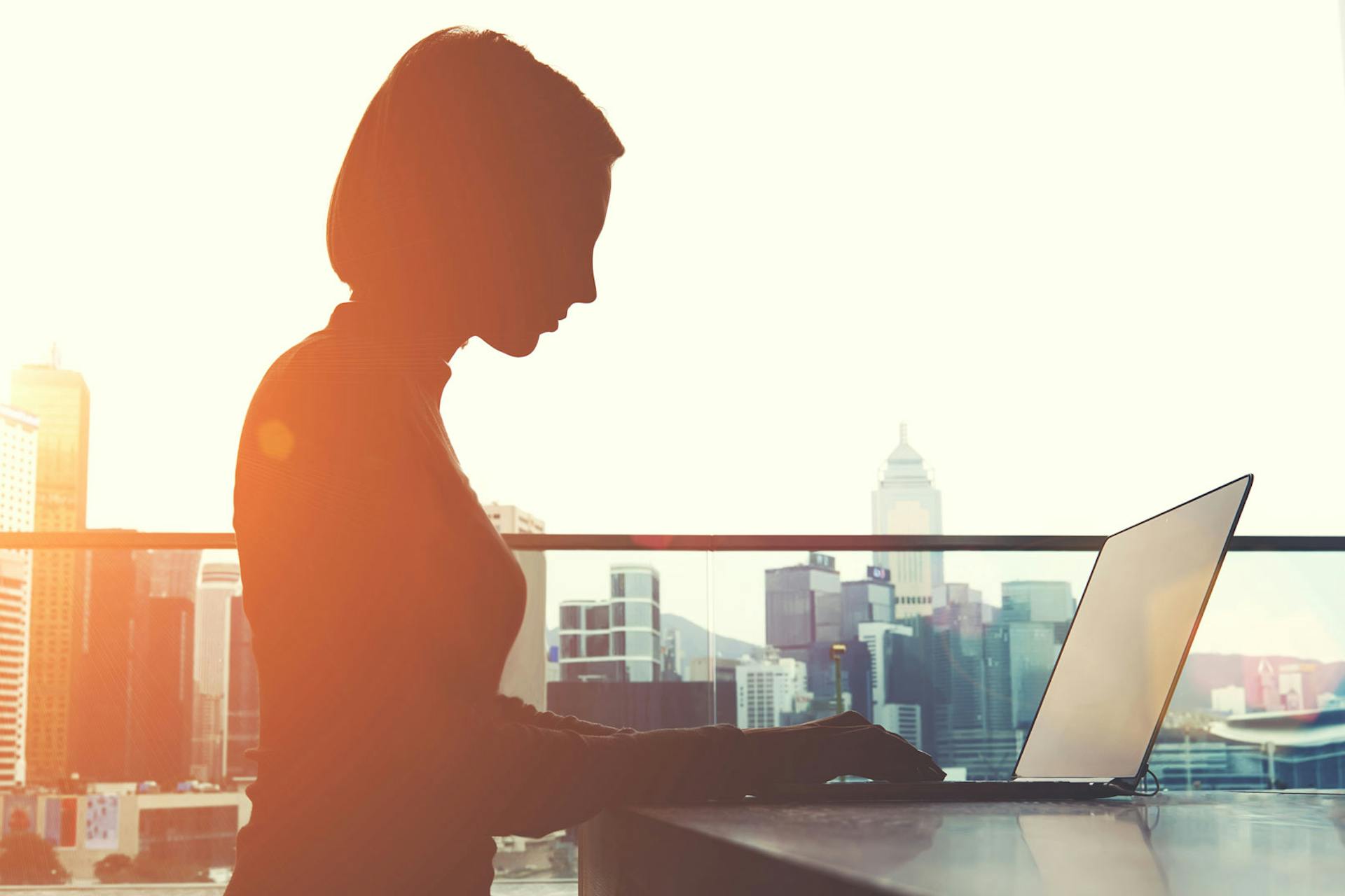 Photo of a woman sitting in front of her laptop on a rooftop terrace in the sunset