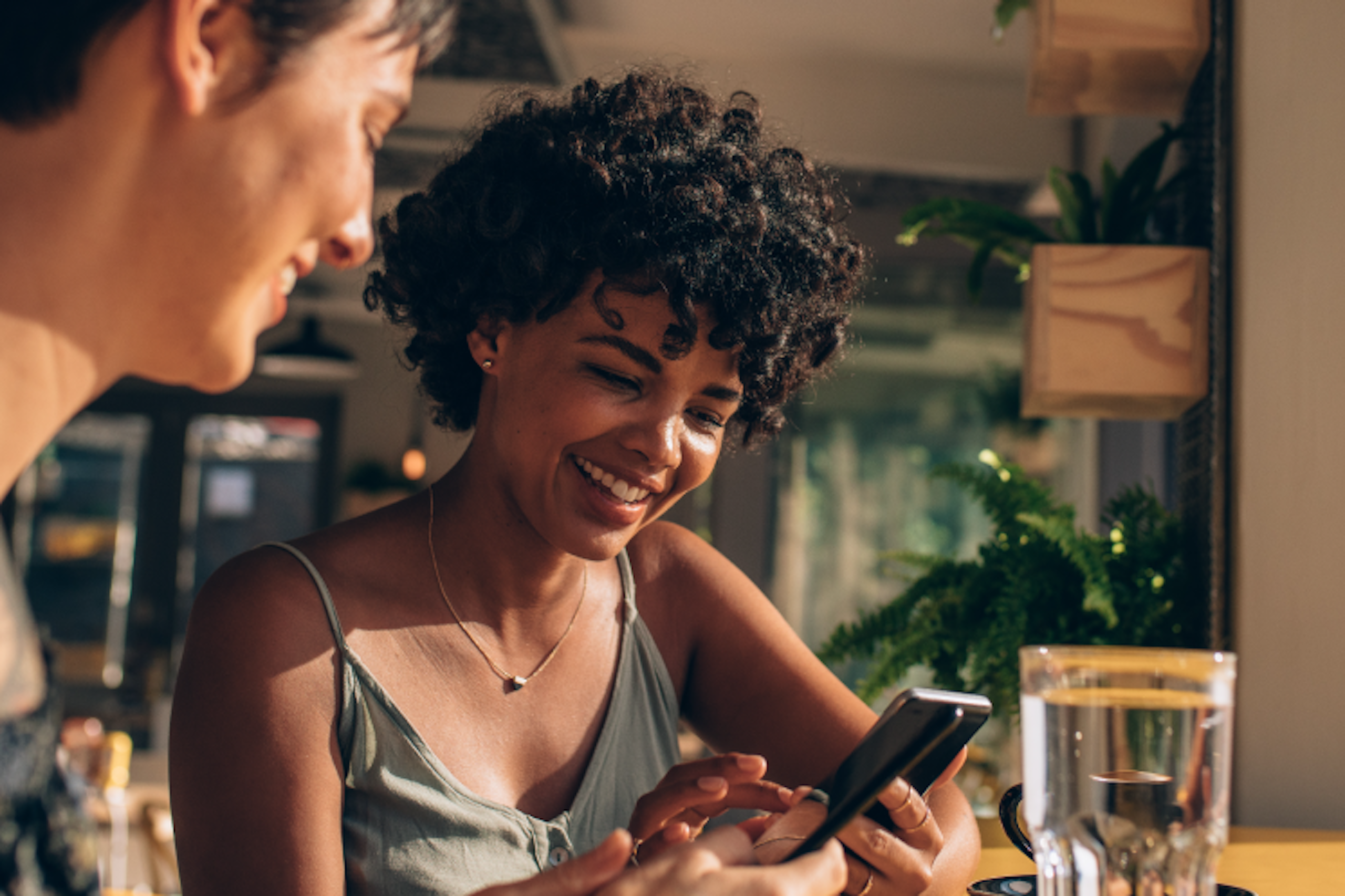 Two people sitting at a table looking at a smart-phone and smiling