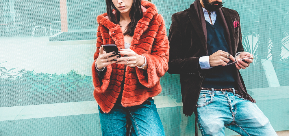 Two fashionable models in textured jackets looking at their smartphones