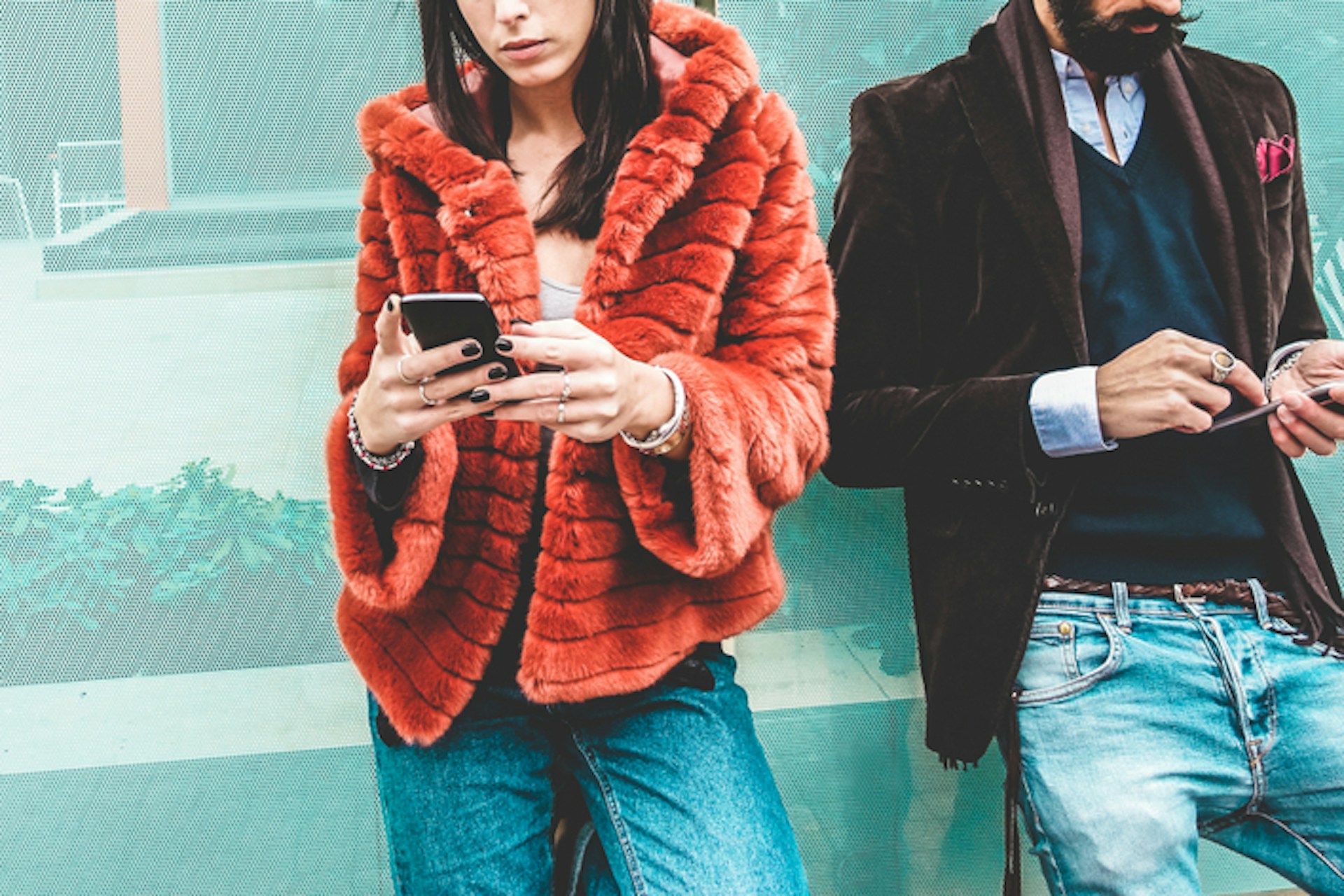 Two fashionable models in textured jackets looking at their smartphones
