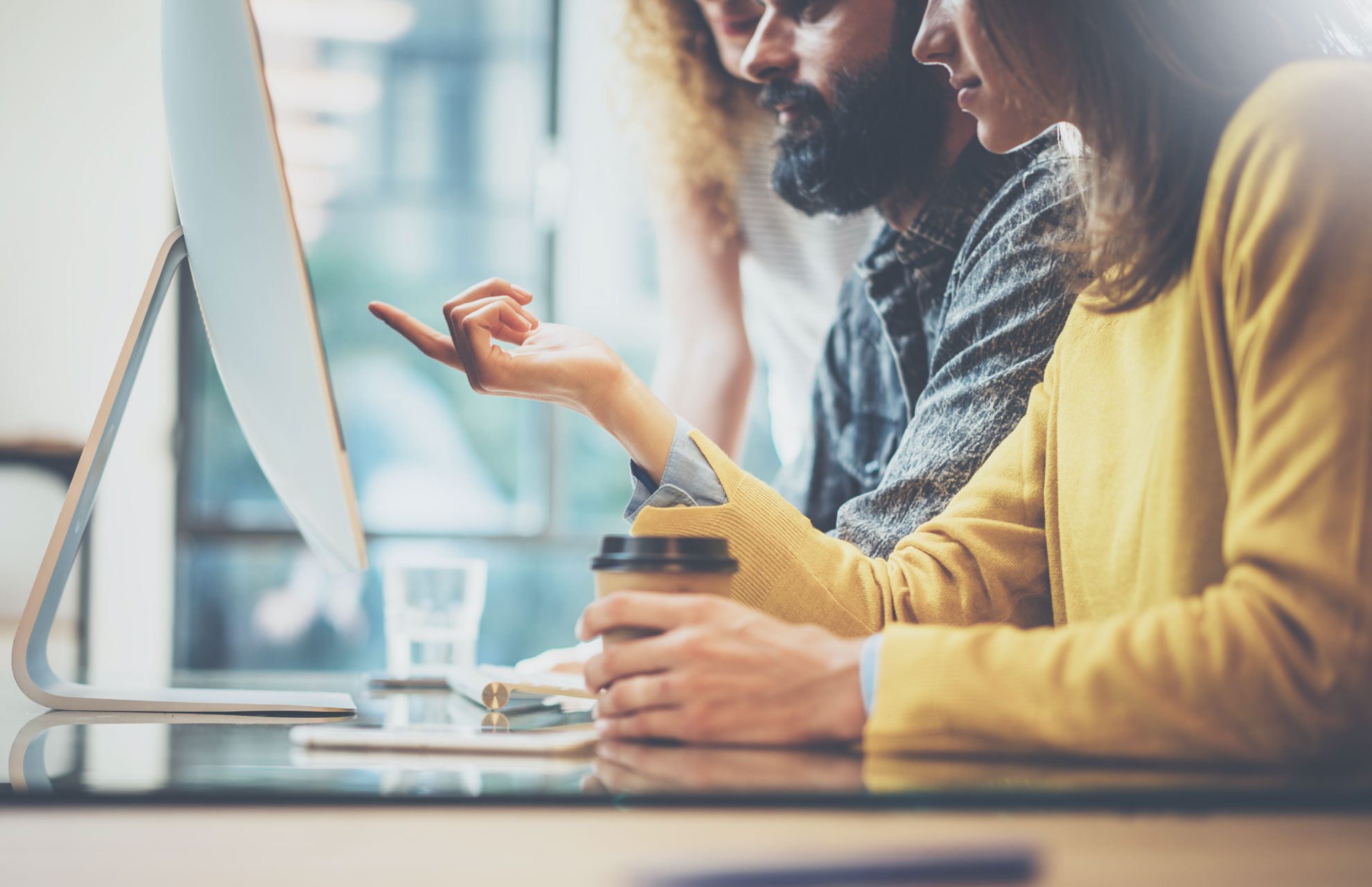 Photo of three people in an office looking at a desktop computer screen
