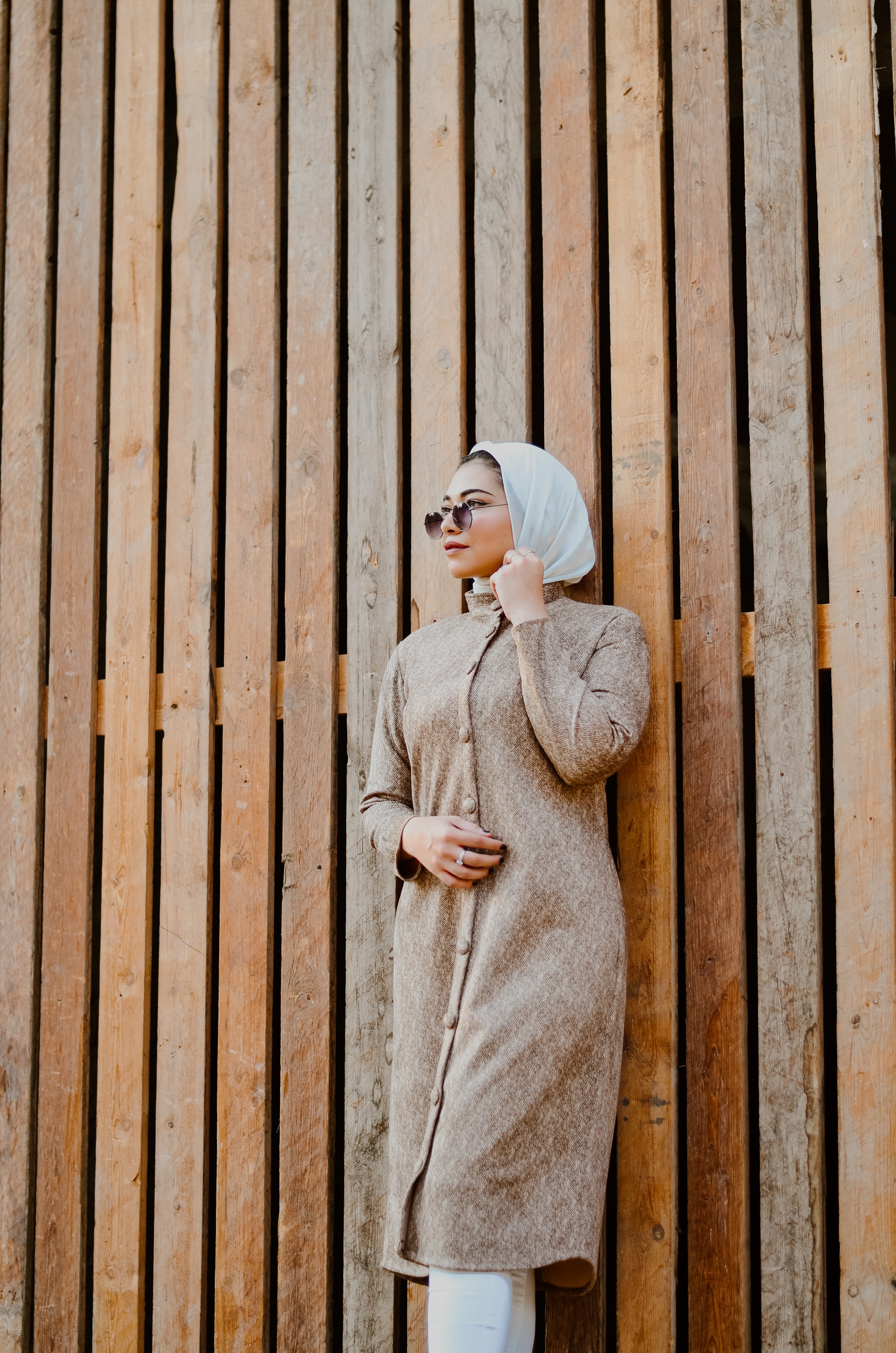 arab woman wearing sunglasses standing against wooden wall