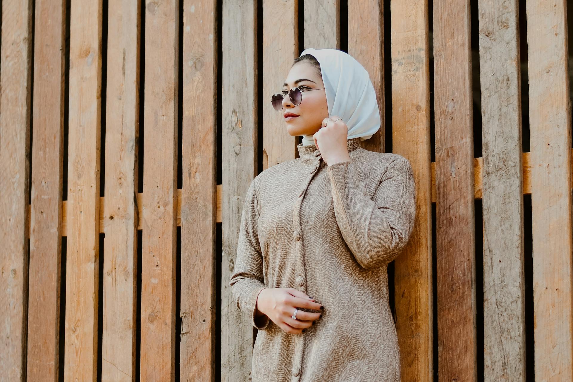 阿拉伯妇女戴着墨镜，靠木墙站着