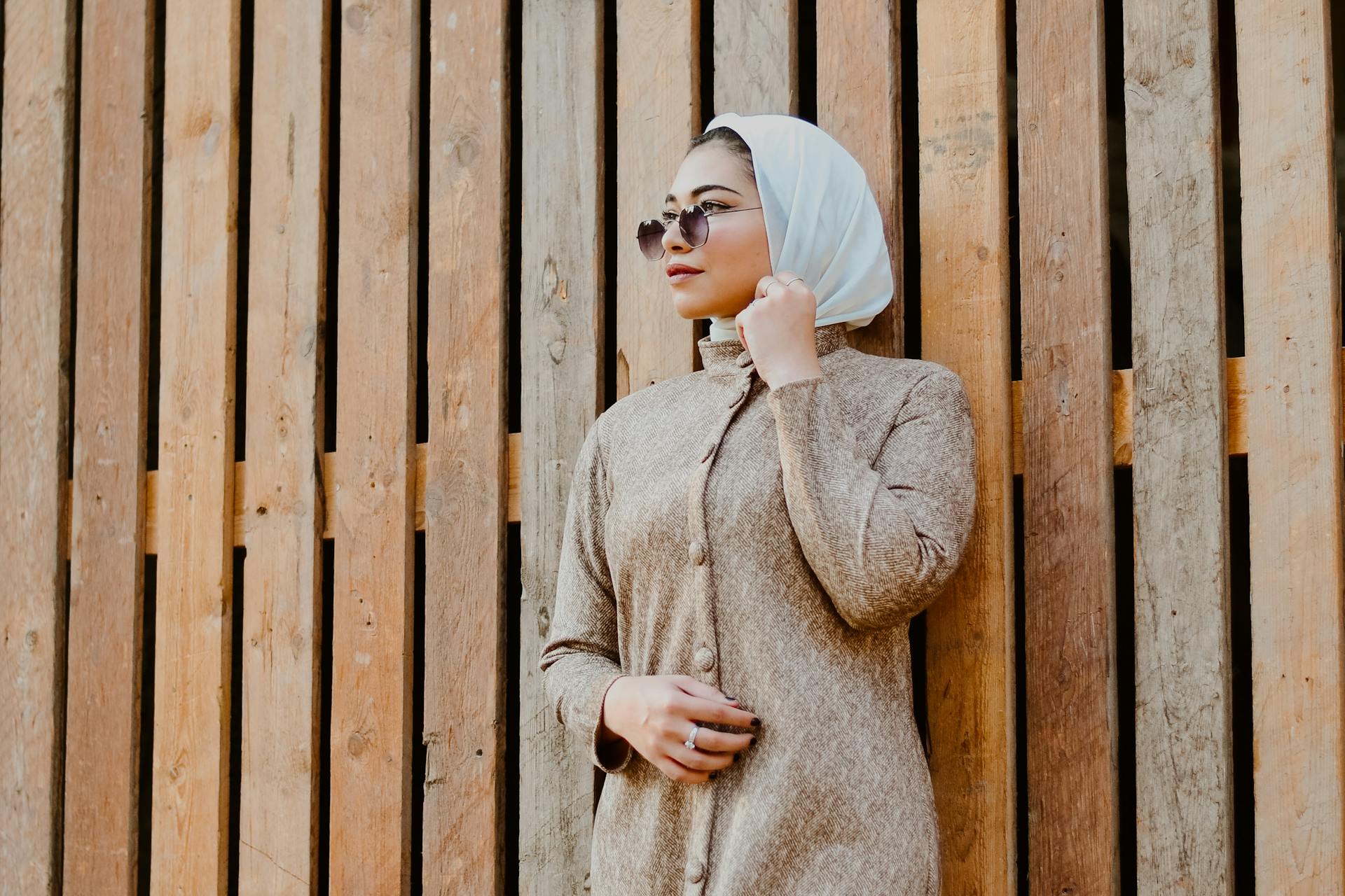 arab woman wearing sunglasses standing against wooden wall