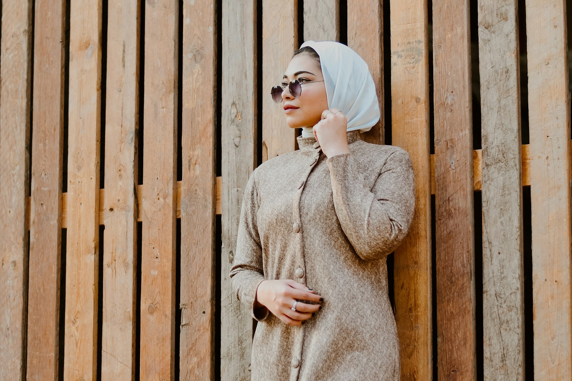 arab woman wearing sunglasses standing against wooden wall