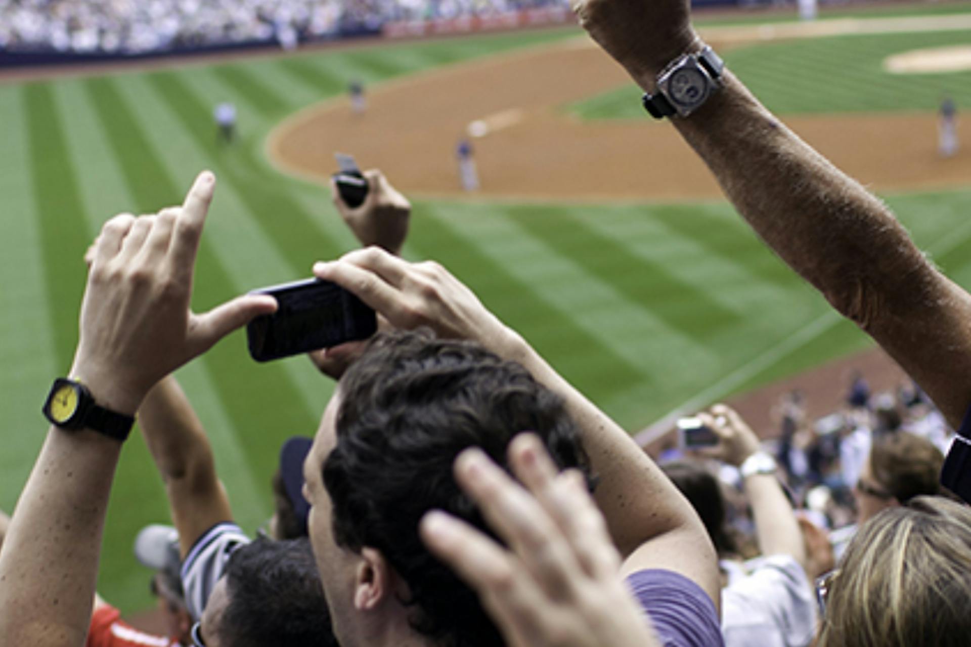 People in the crowd of a baseball game recording on their phone and cheering 