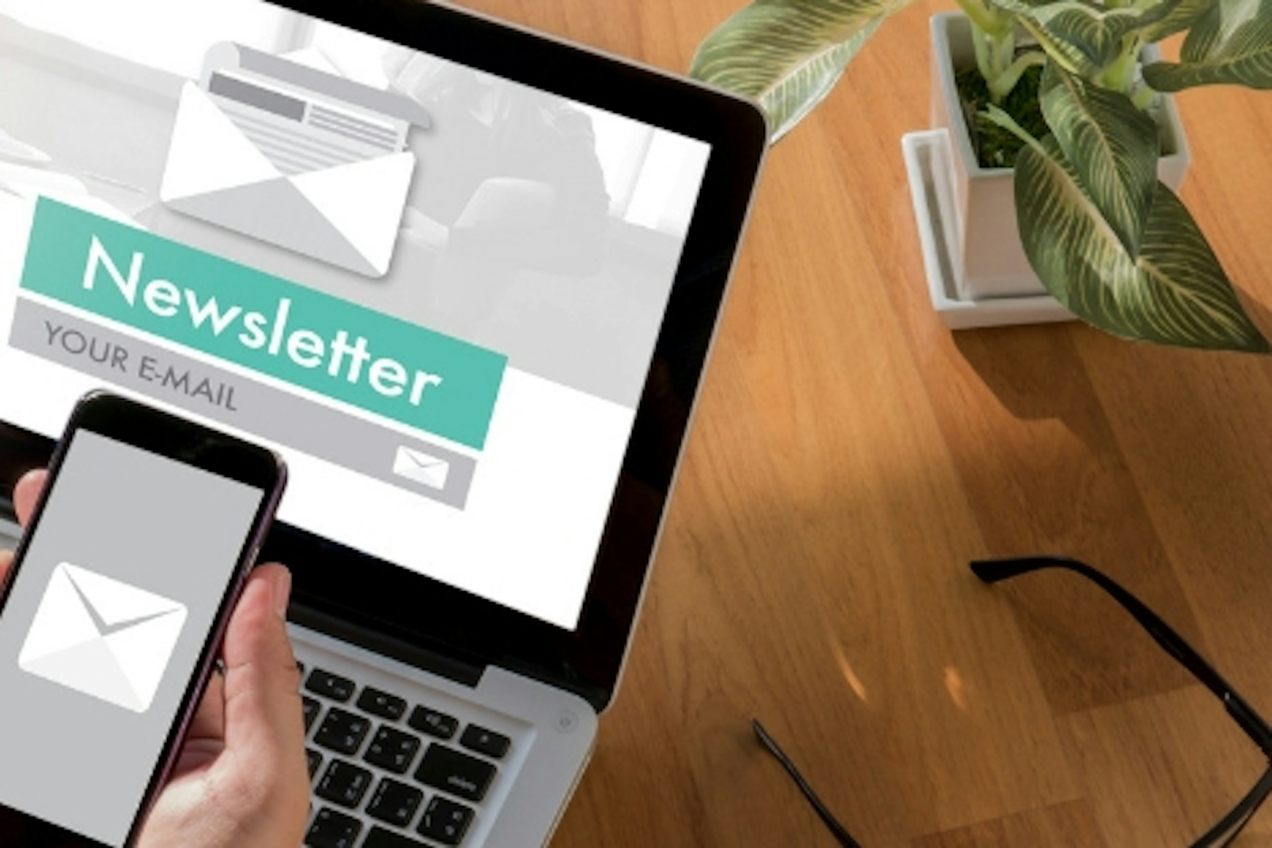 Foto Laptop und Smartphone auf Tisch mit Newsletter Screen Icons