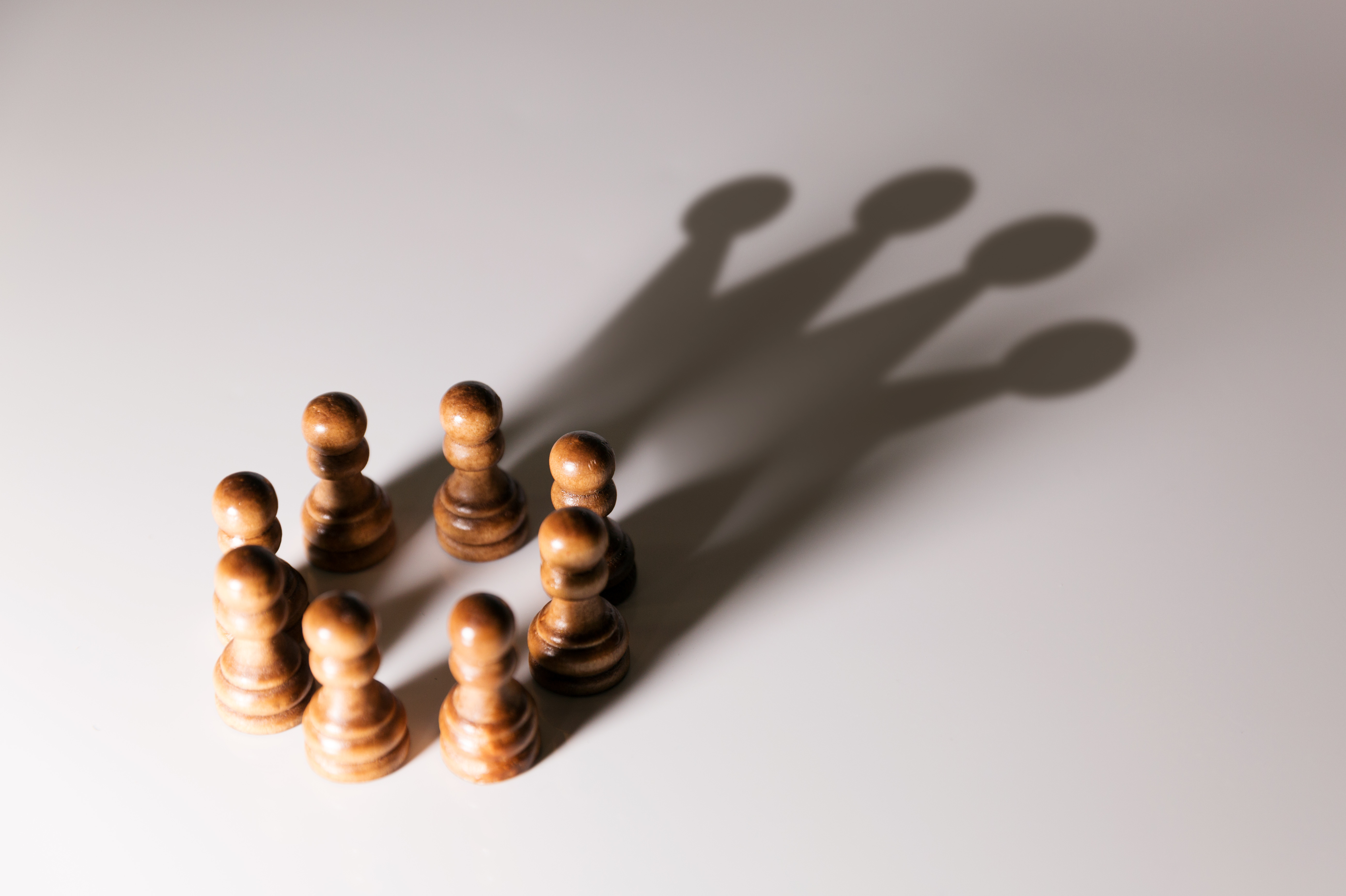 Chess pawns in a circle, with a shadow projecting the image of a crown.