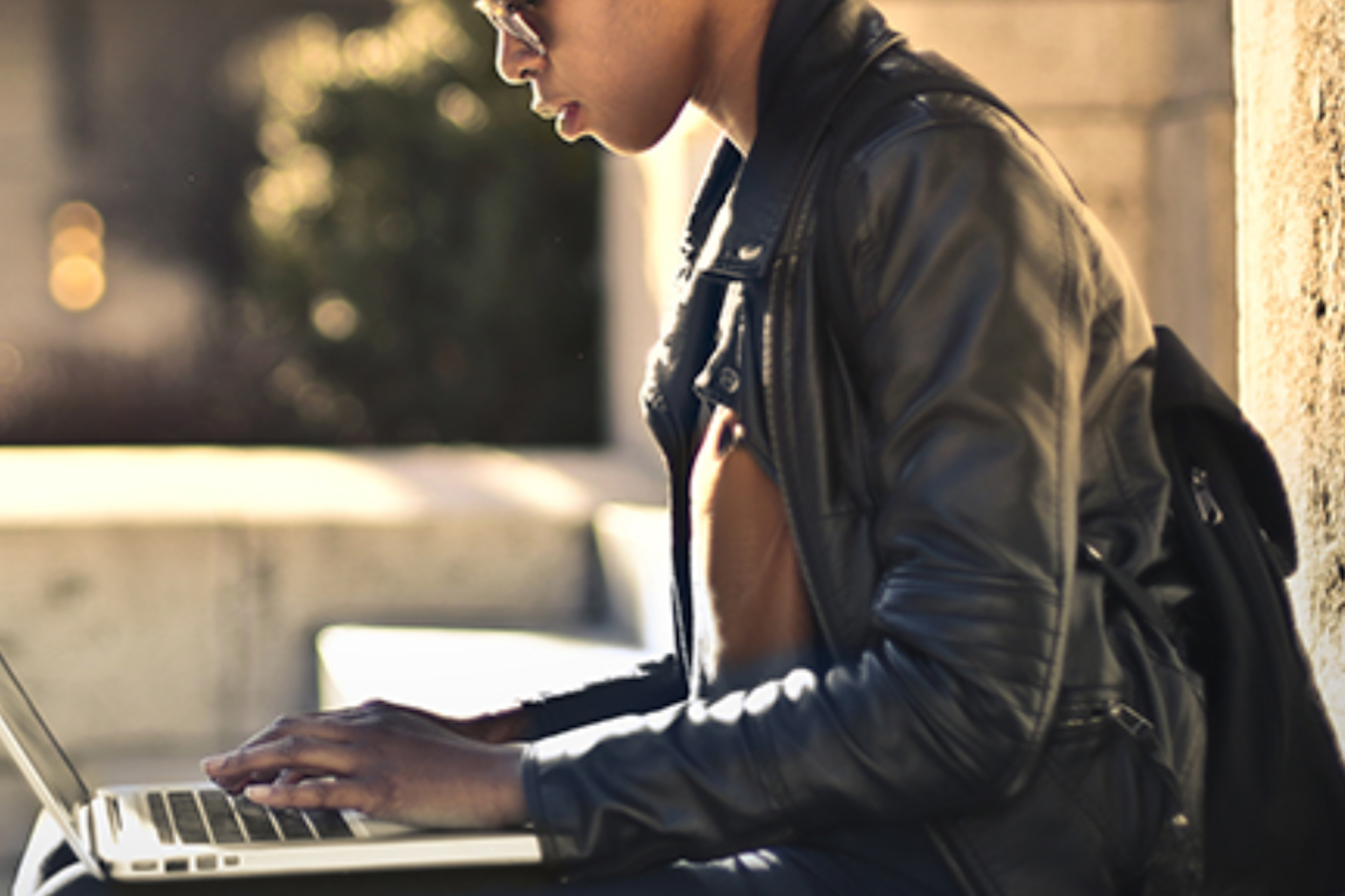 Side view of a girl in a leather jacket using a laptop