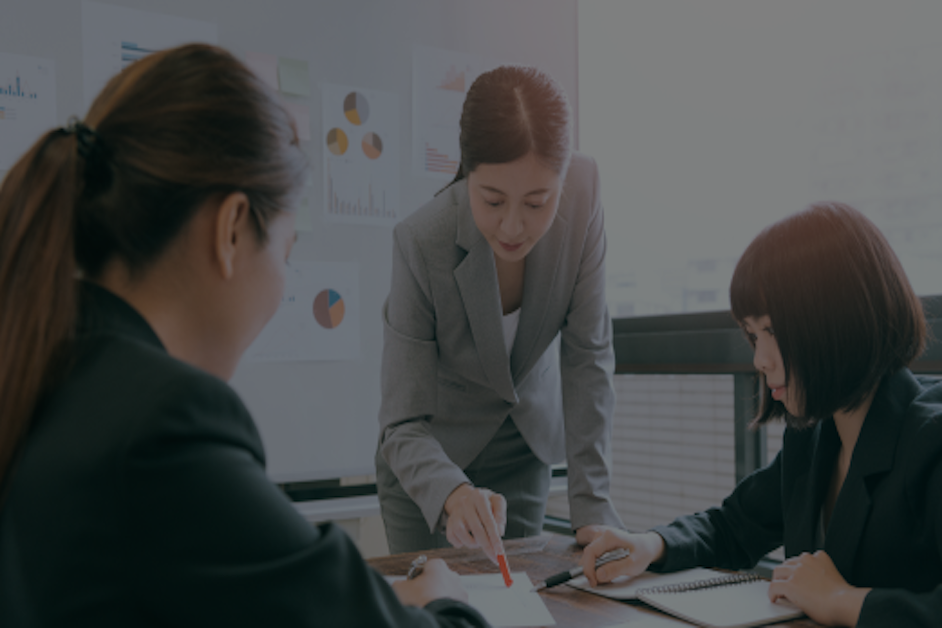 three woman wearing suits in a boardroom looking at notes on the table