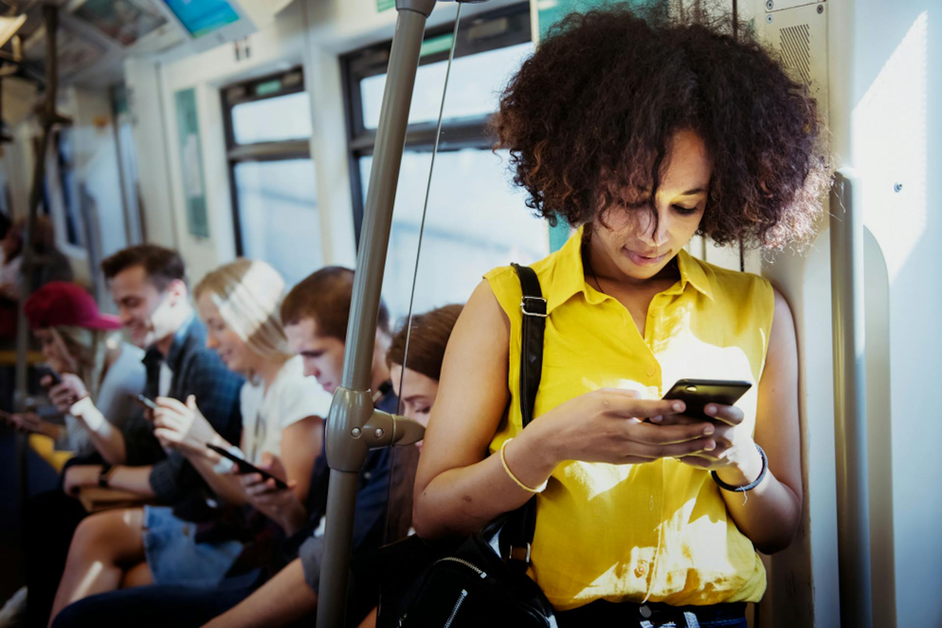 Junge Frau im Vordergrund in der Bahn an ihrem Smartphone, junge Menschen im Hintergrund an ihren Smartphones