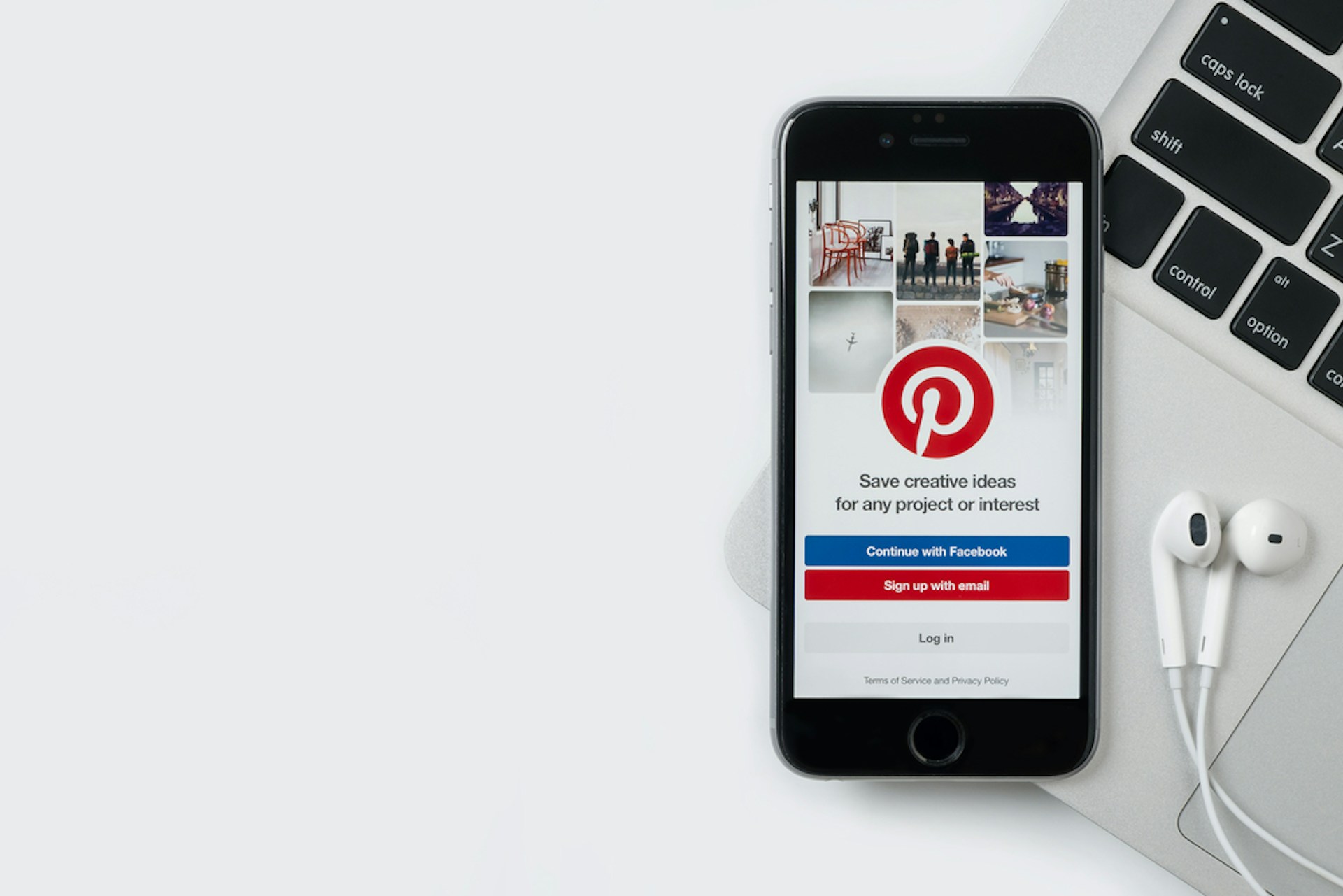 Un smartphone affichant la page de connexion Pinterest est posé sur un ordinateur portable à côté duquel on apperçoit des écouteurs