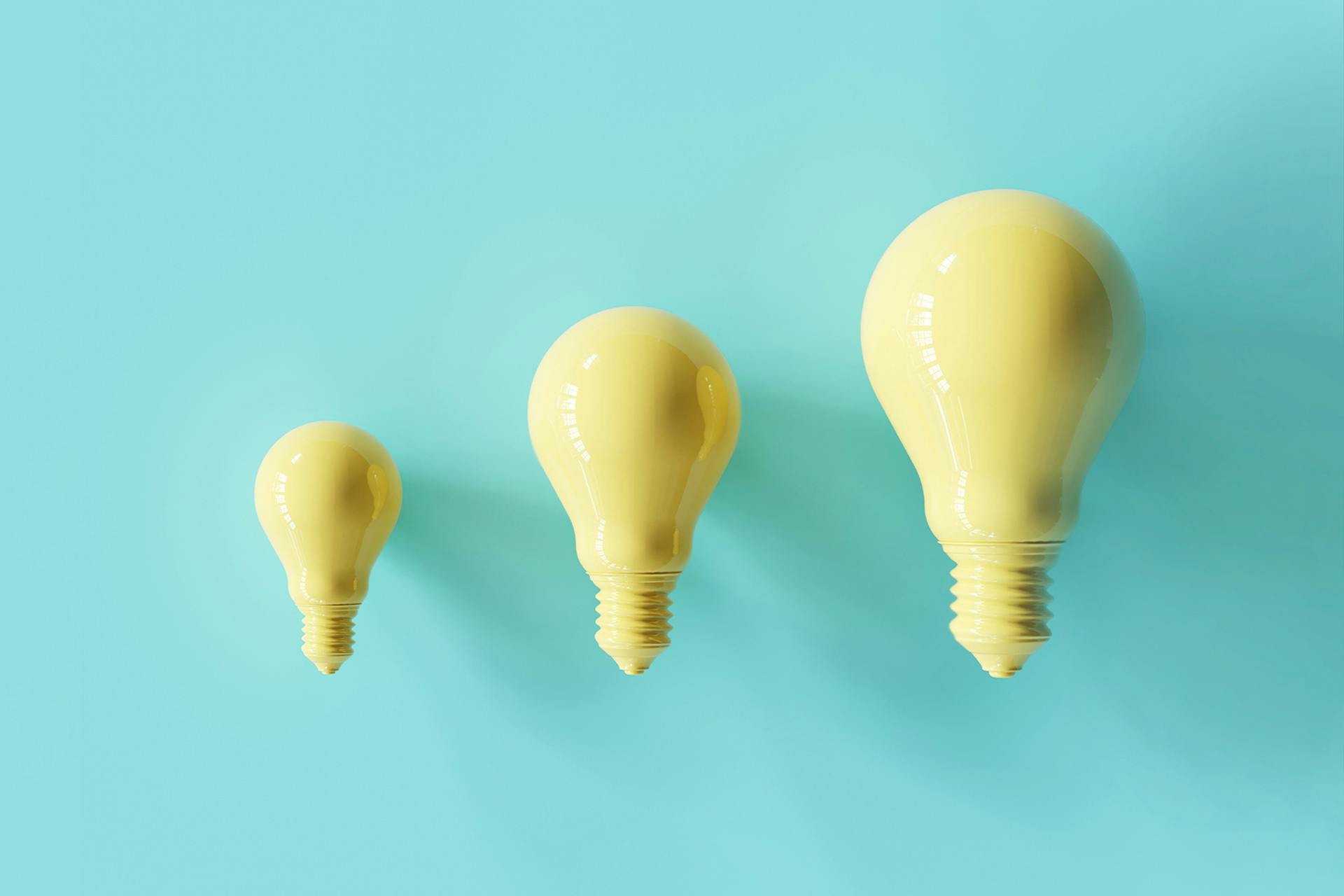 Three yellow lightbulbs lined up next to one another. The lightbulbs are three different sizes, but all the same shape. 