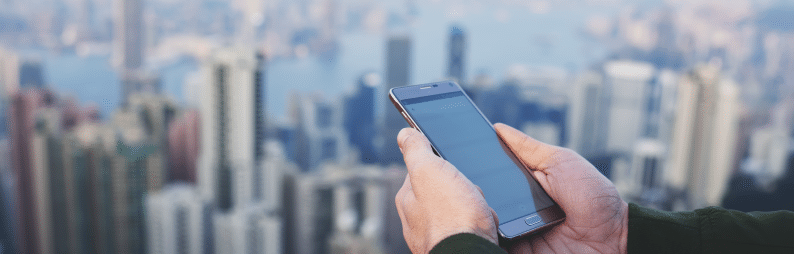 Hand holding a phone with buildings in the background.