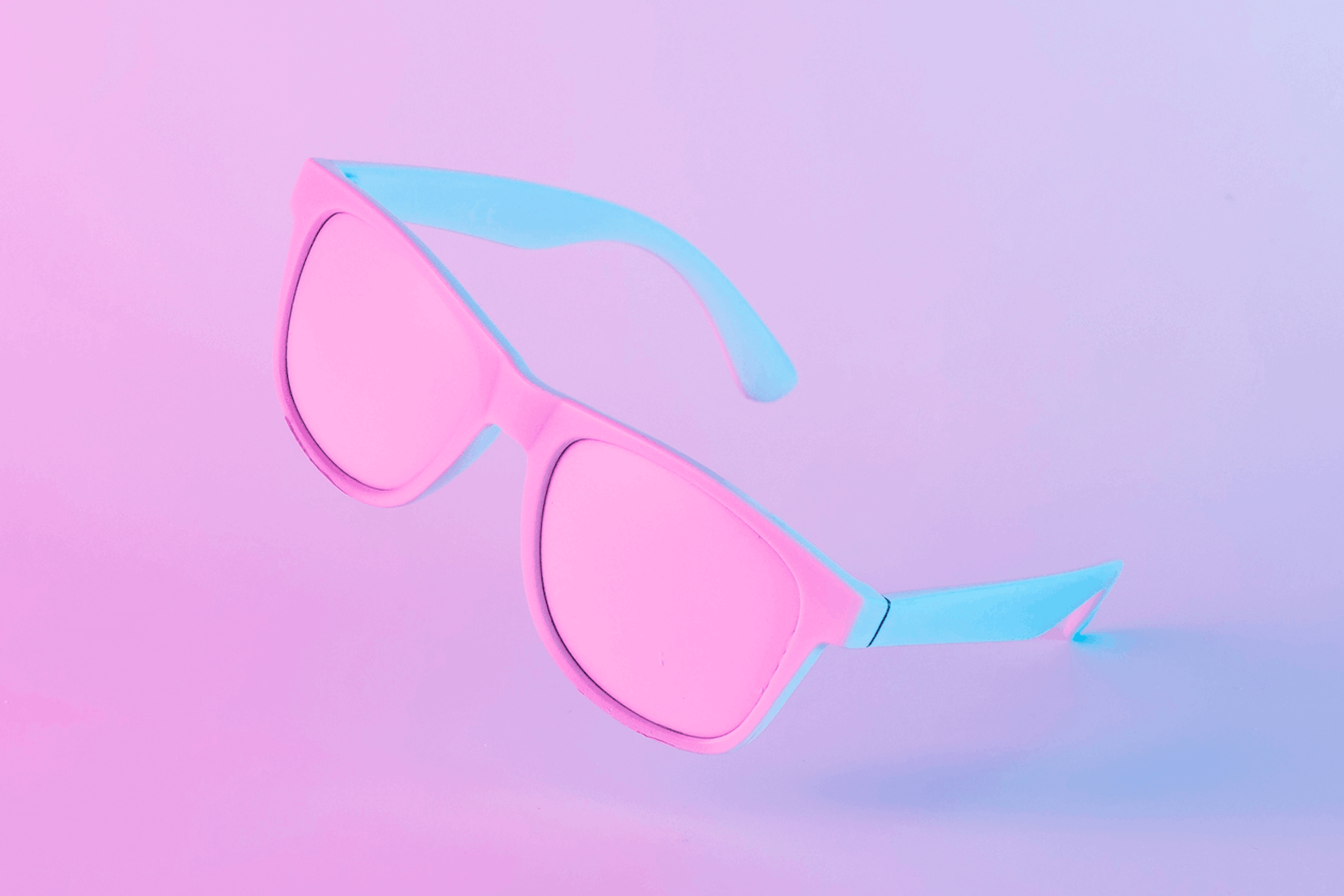 A pair of pink and blue sunglasses on a pink background. The sunglasses appear ad if they are being photographed for a fashion photoshoot that an instagram influencer in South Africa may share on his/her account.