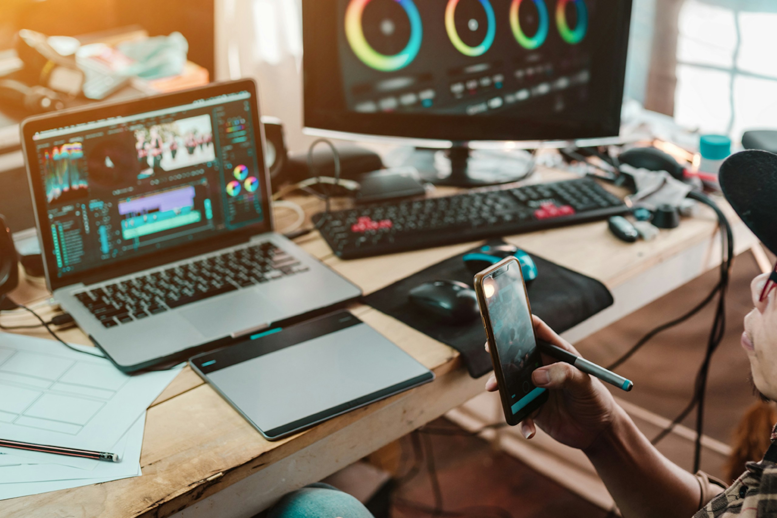 A person holding a smart phone, sitting at a desk full of various pieces of technology for generating and tracking UGC