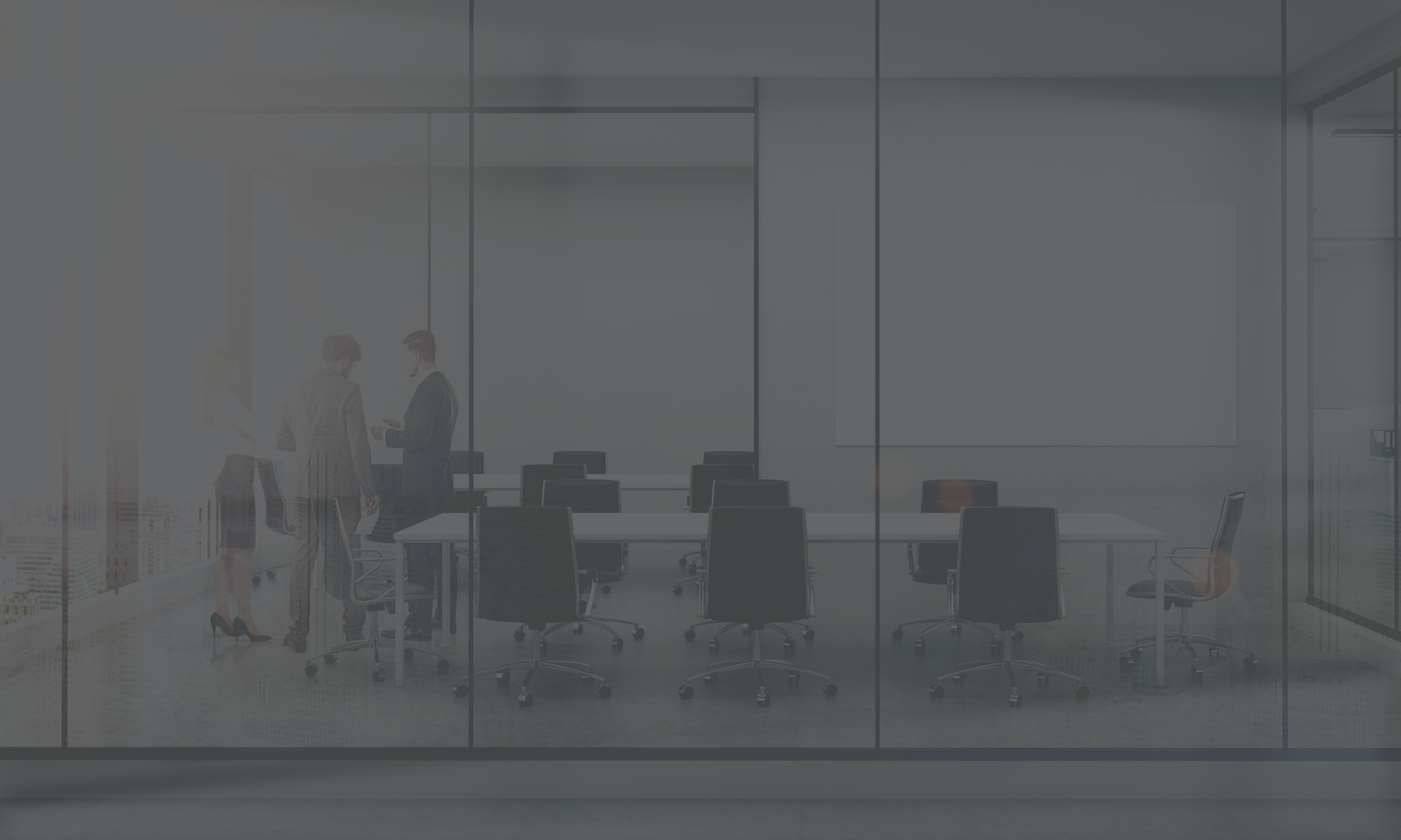 Empty boardroom table and seats, with three people talking at one end.
