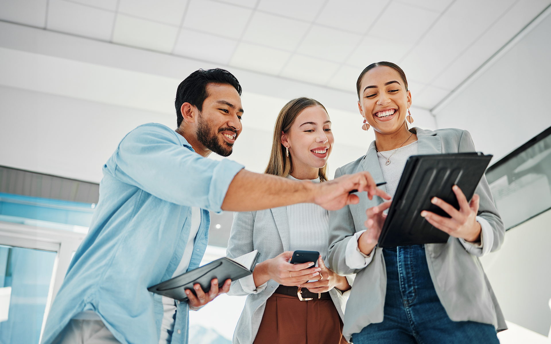 Un groupe de spécialistes du marketing des médias sociaux heureux dans un bureau, regardant et pointant une tablette.