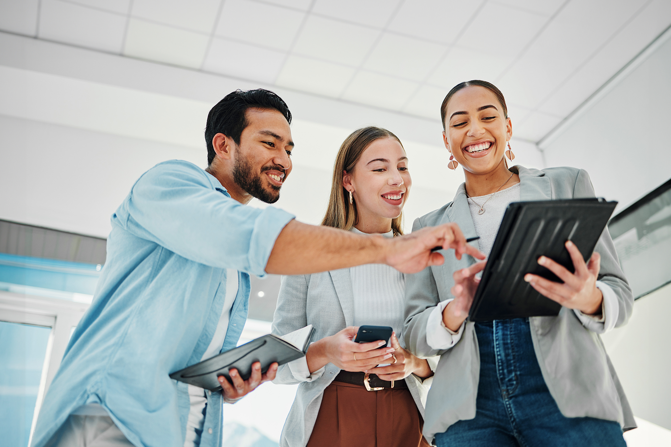 Un groupe de spécialistes du marketing des médias sociaux heureux dans un bureau, regardant et pointant une tablette.