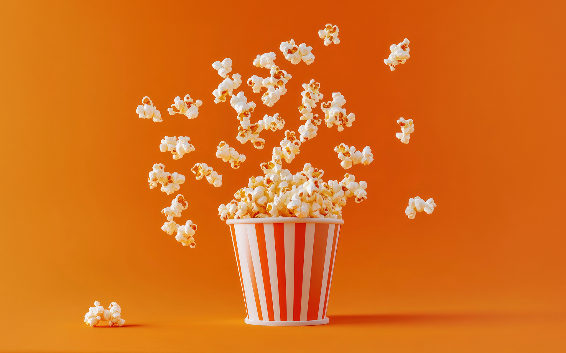 Popcorn exploding out of a red and white striped movie theater popcorn bucket 