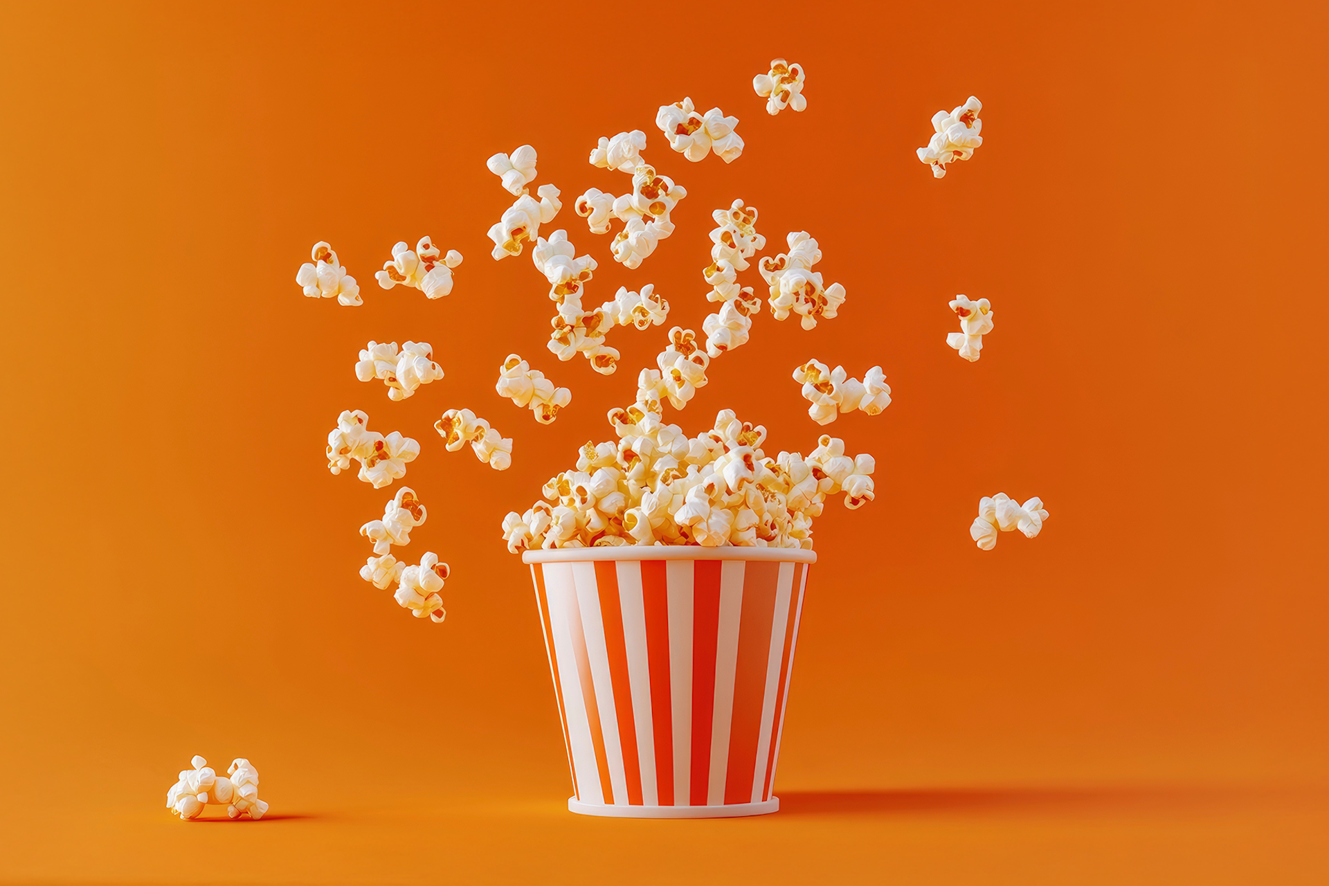 Popcorn exploding out of a red and white striped movie theater popcorn bucket