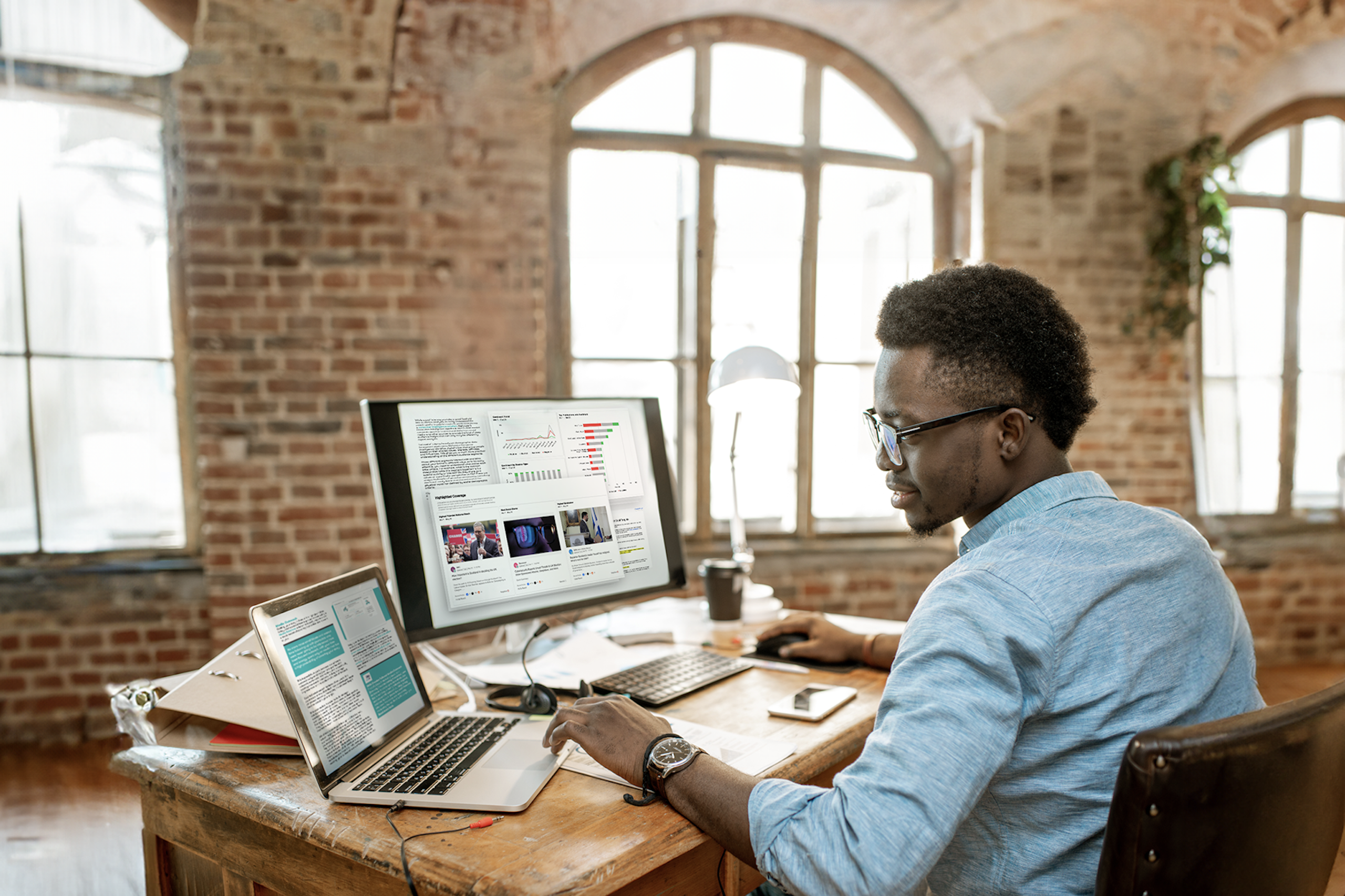 Image d'un professionnel des relations publiques assis à son bureau devant un grand écran et un ordinateur portable. Les ordinateurs affichent divers tableaux et outils destinés aux professionnels des relations publiques. Téléchargement de PR Toolkit