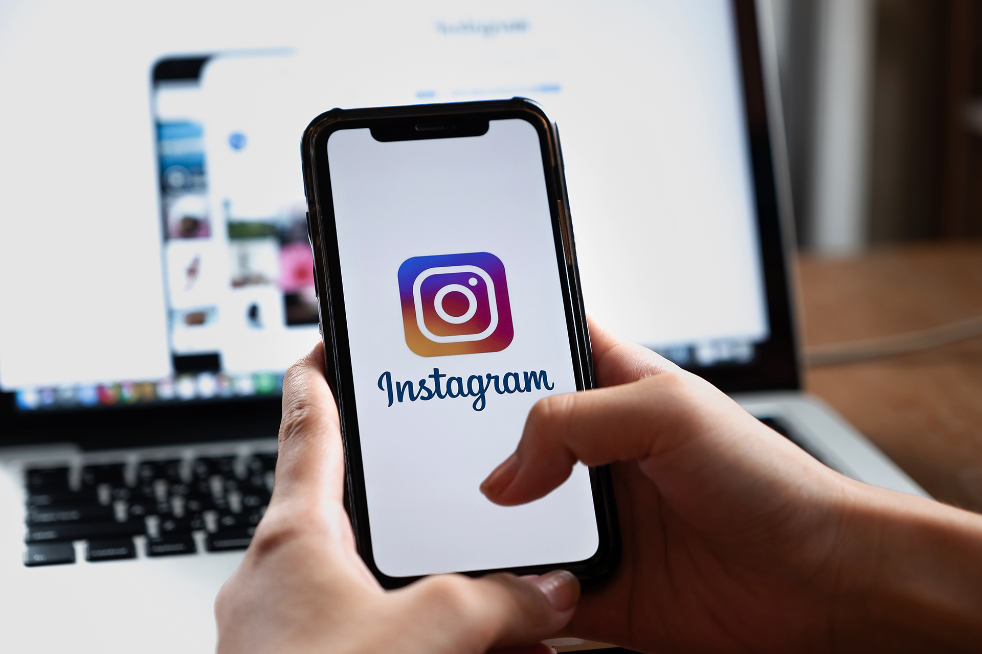 Woman logging into Instagram on her phone. Computer screen in the background.