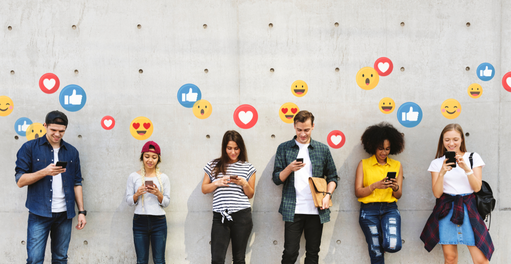 People using smartphones lined up against a wall. Facebook reactions are illustrated above them