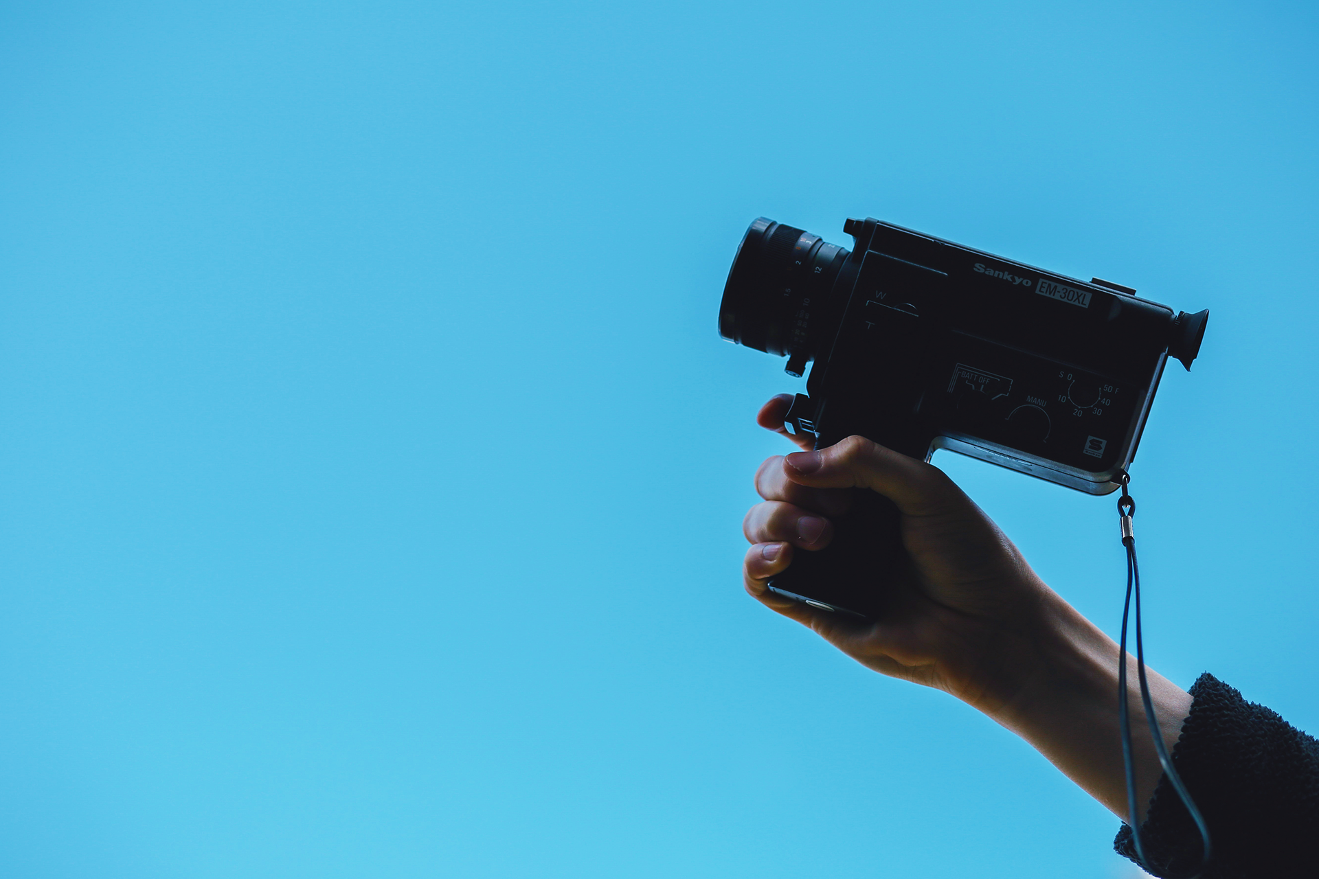 Woman's hand holding a camera like a gun over a blue background.