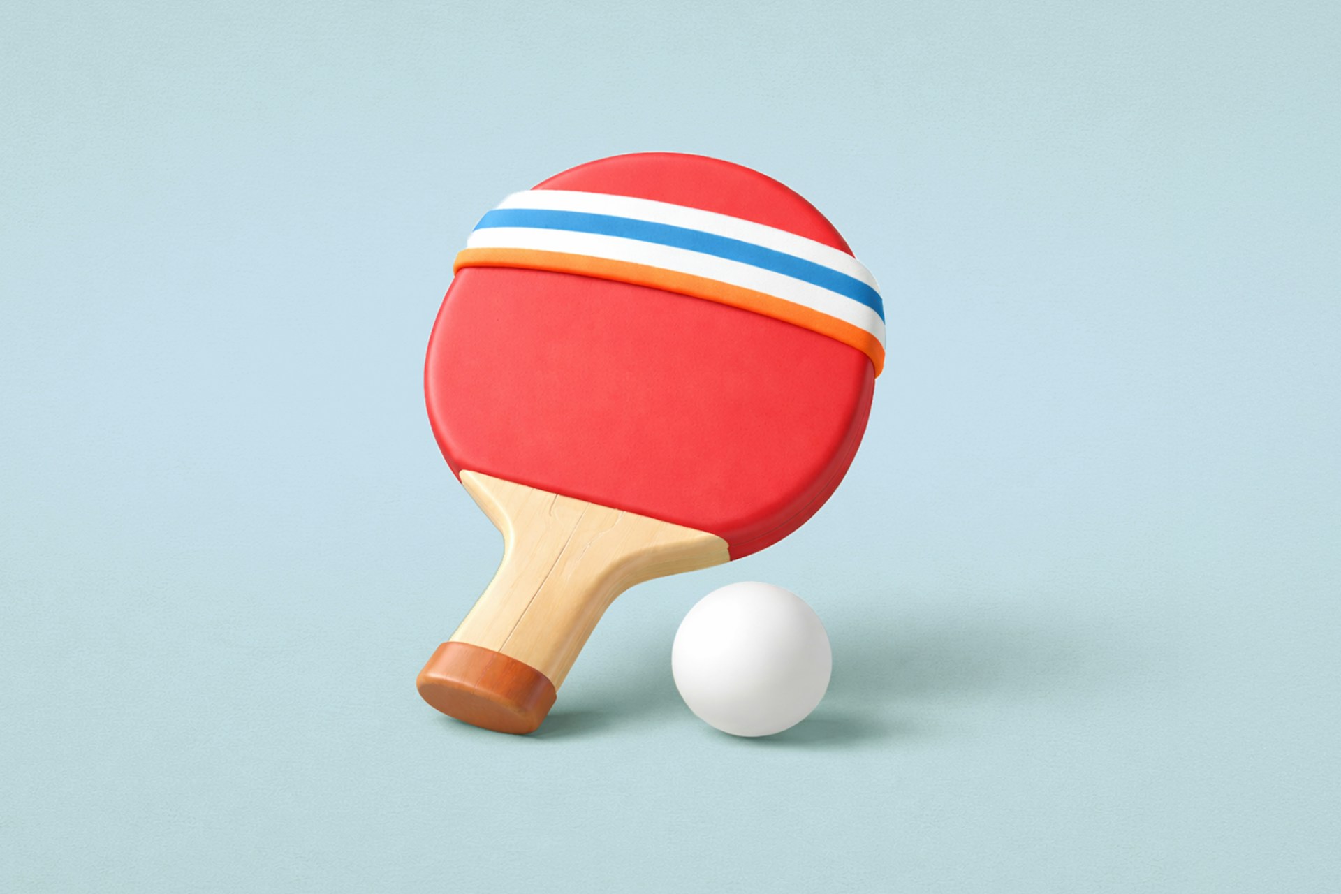 A white ping pong ball beside a red ping pong paddle against a light blue background.