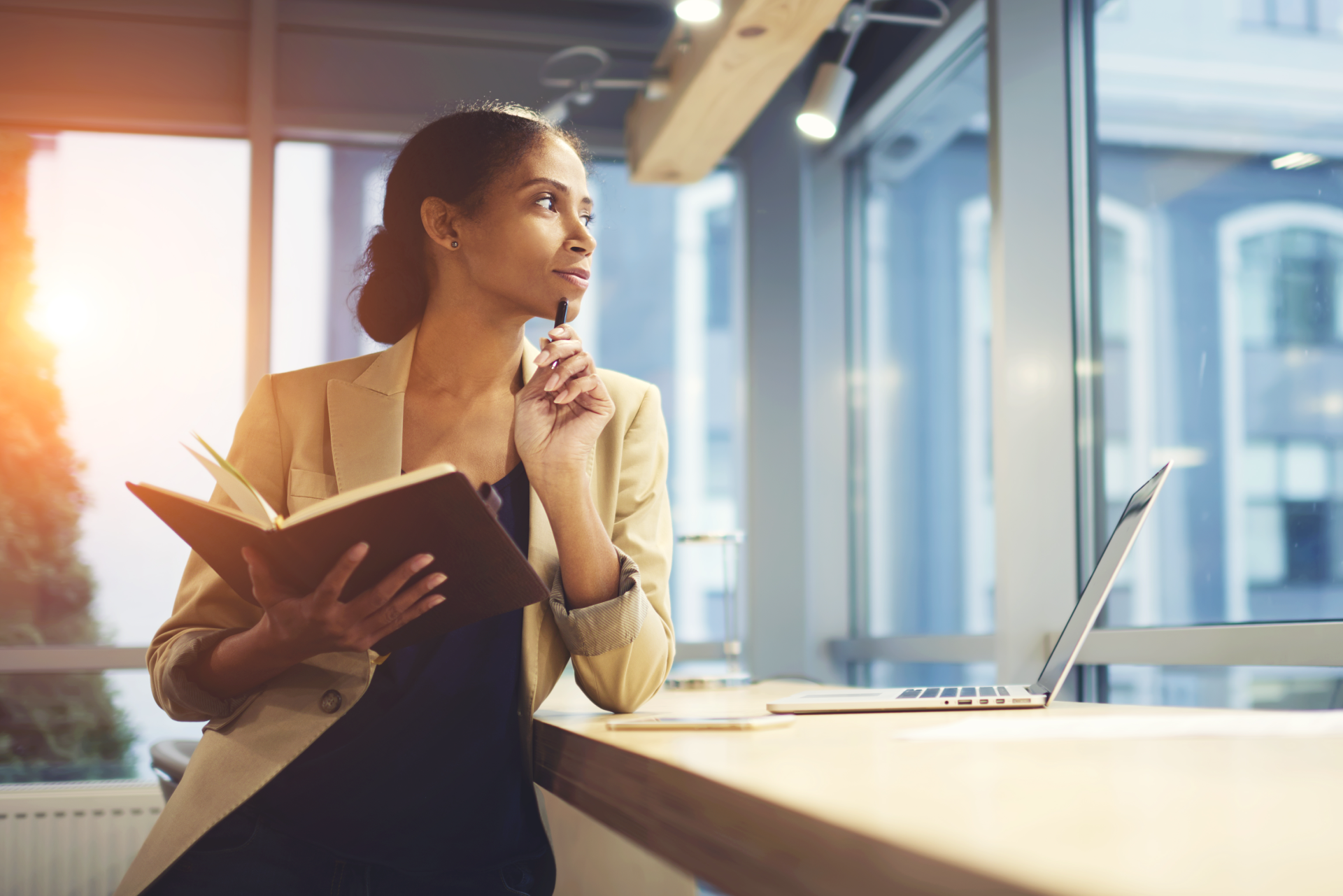woman thinking and holding a note pad while looking outside the office window