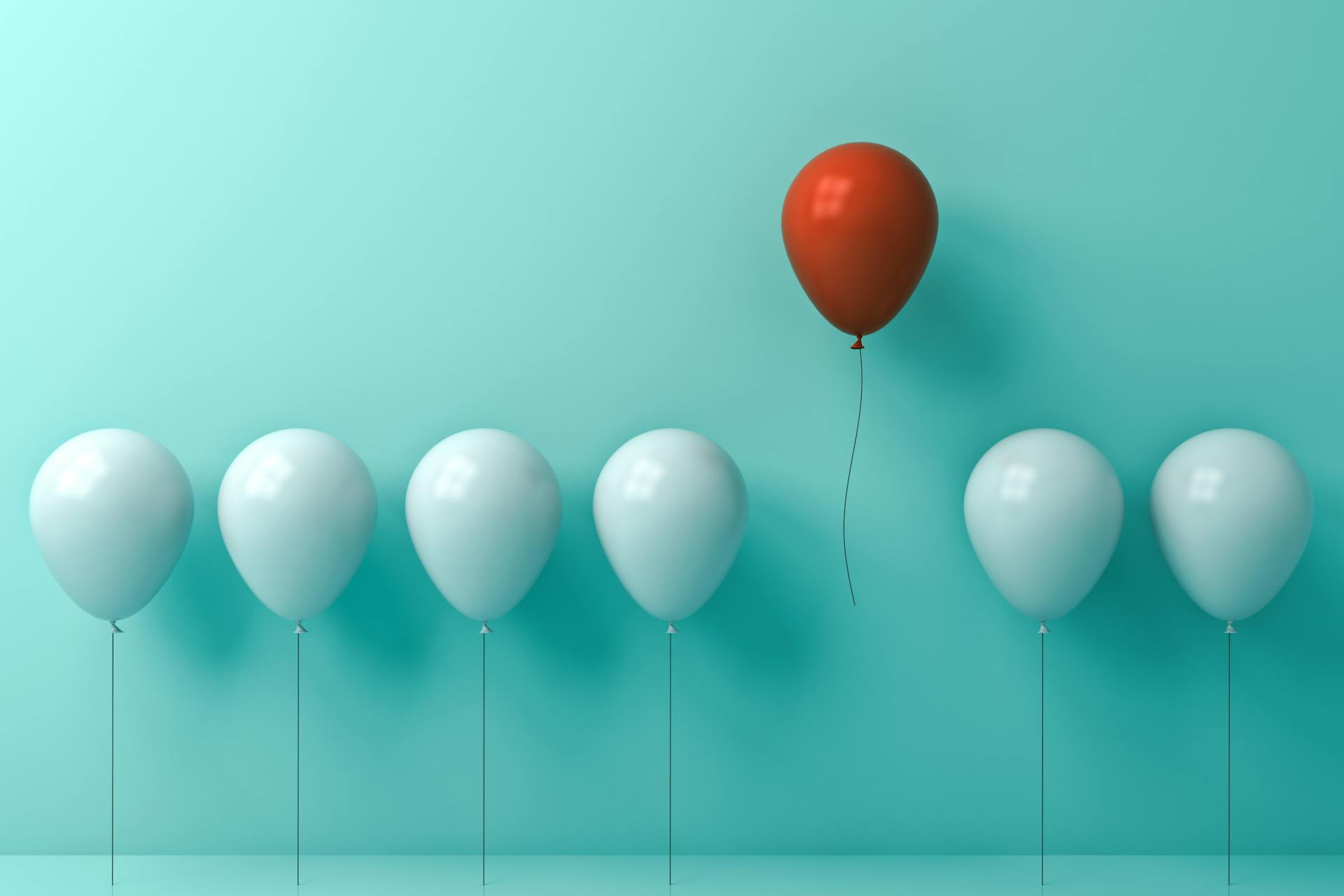 Image of white balloons with one red balloon flying away 