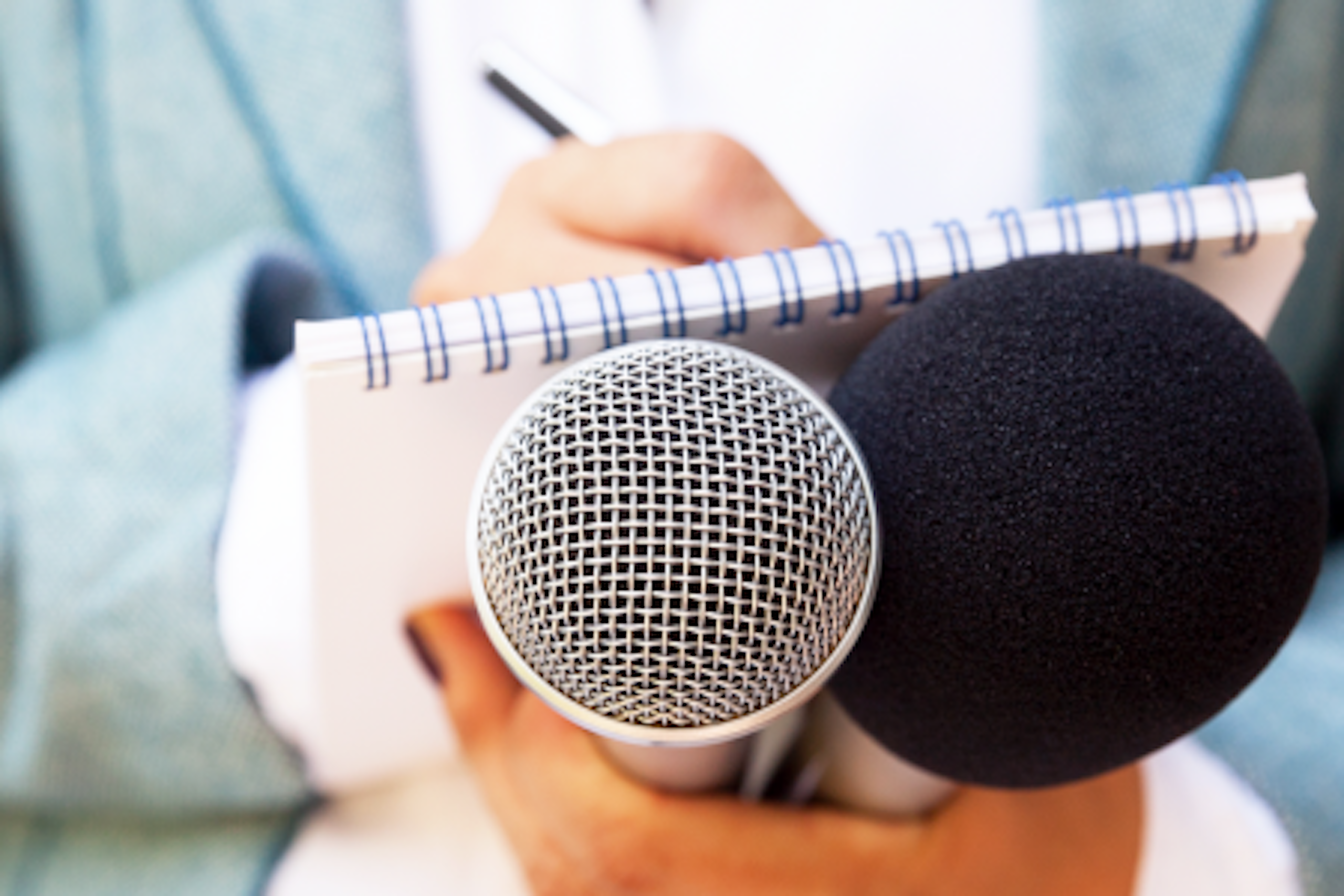 A reporter writing in a notepad while holding two microphones