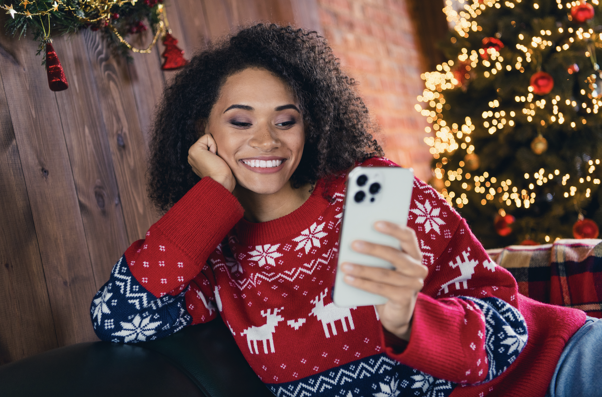 A photo of a woman in a Christmas sweater checking her smartphone
