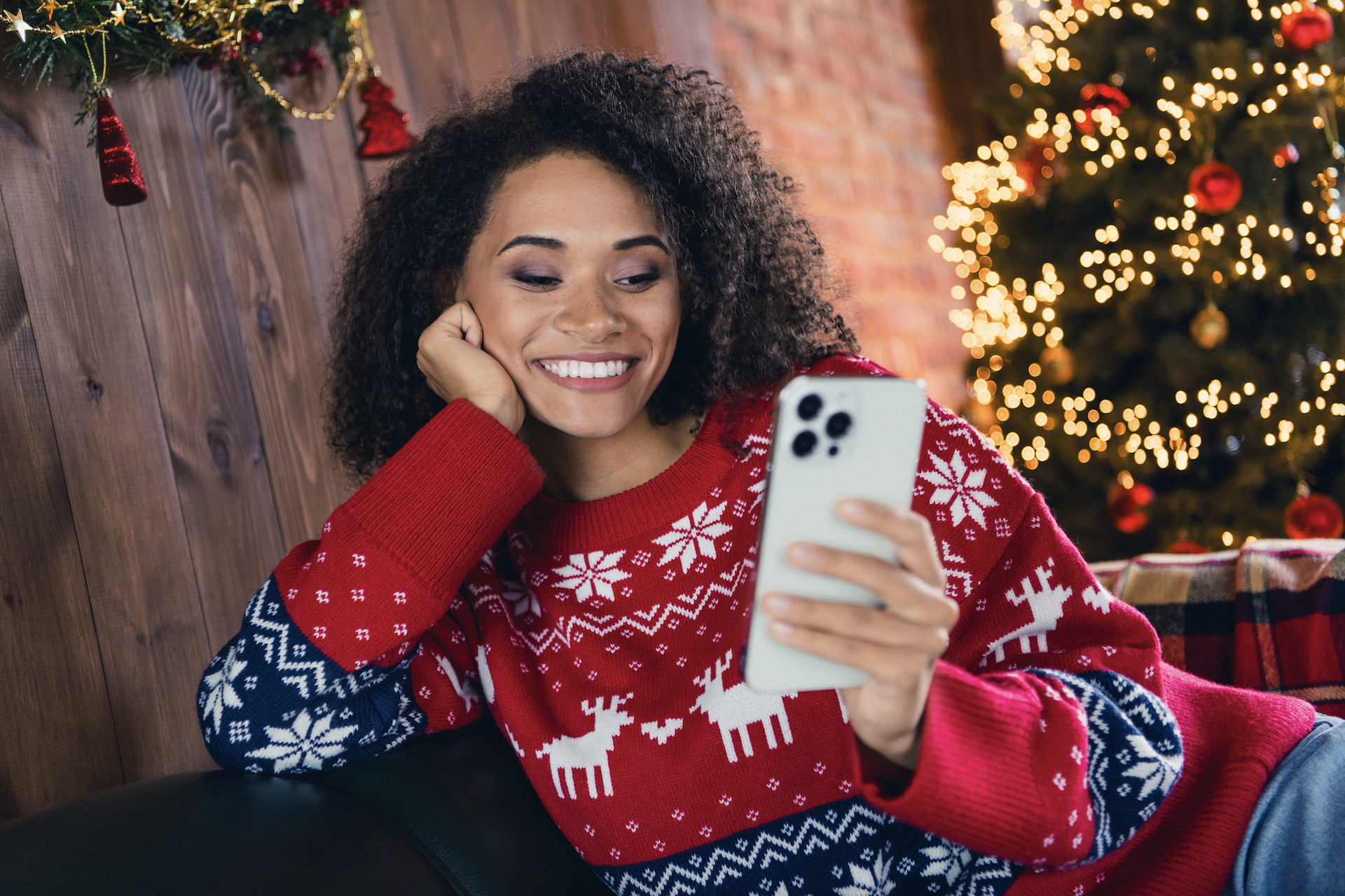 A photo of a woman in a Christmas sweater checking her smartphone