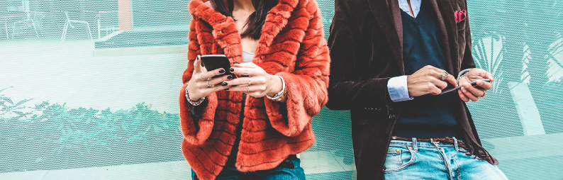 two people in fashion clothing holding mobile phones