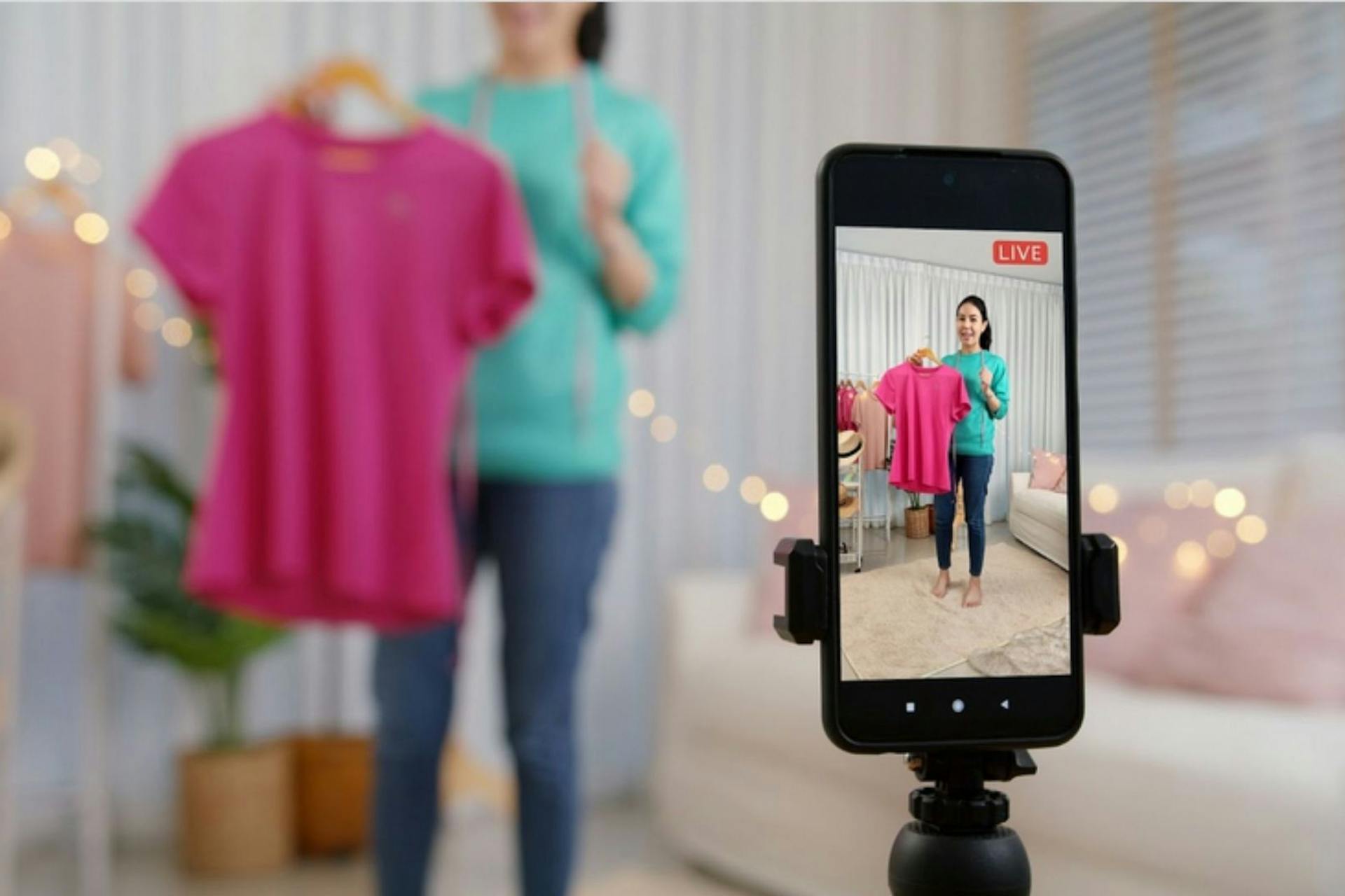 Smartphone sur un trépied qui filme une influenceuse qui présente un tshirt rose 