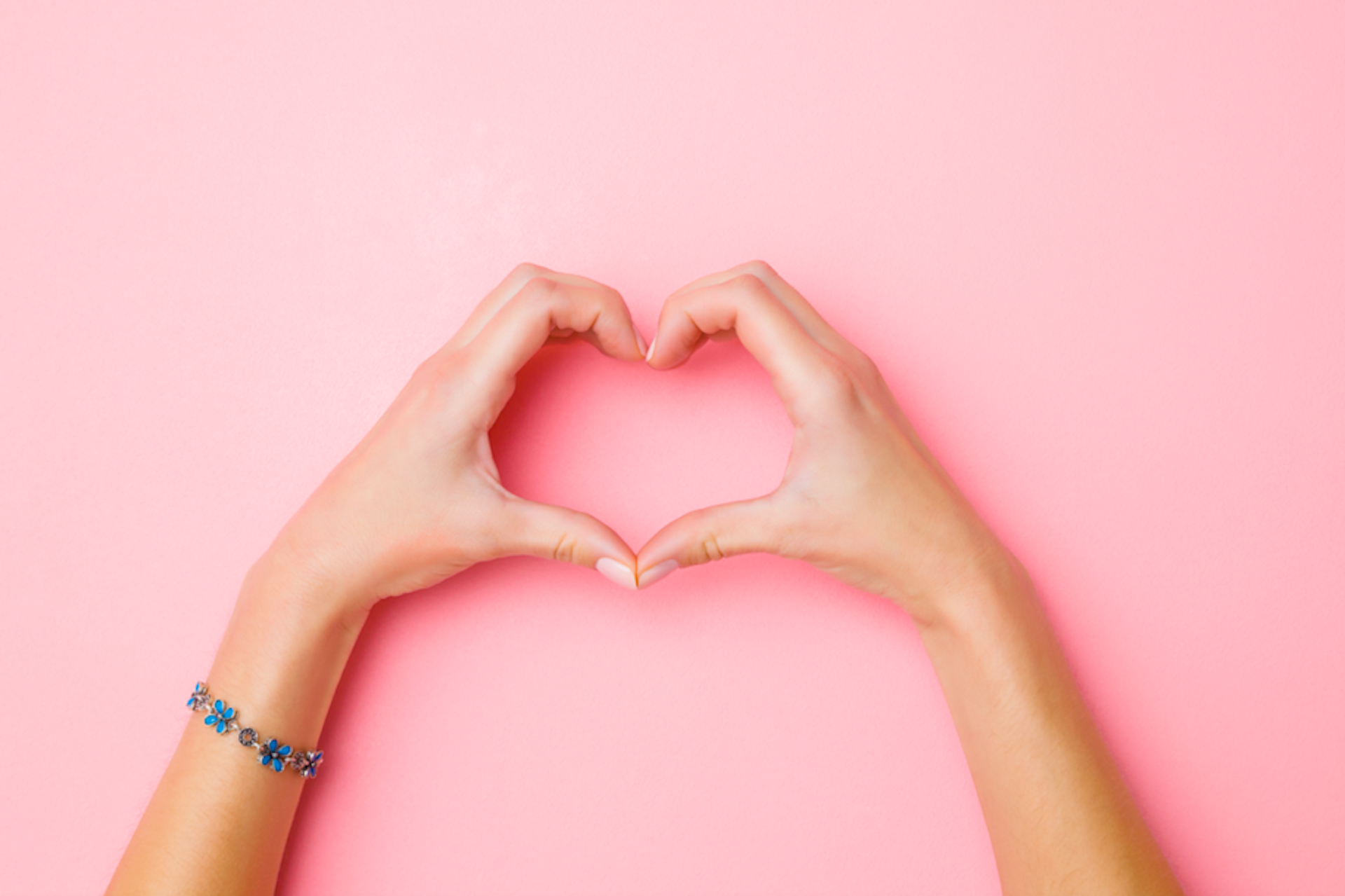 hand creating a heart shape against a pink background