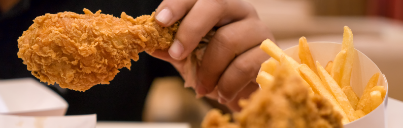 Hand holding a fried chicken drumstick with a black background. 