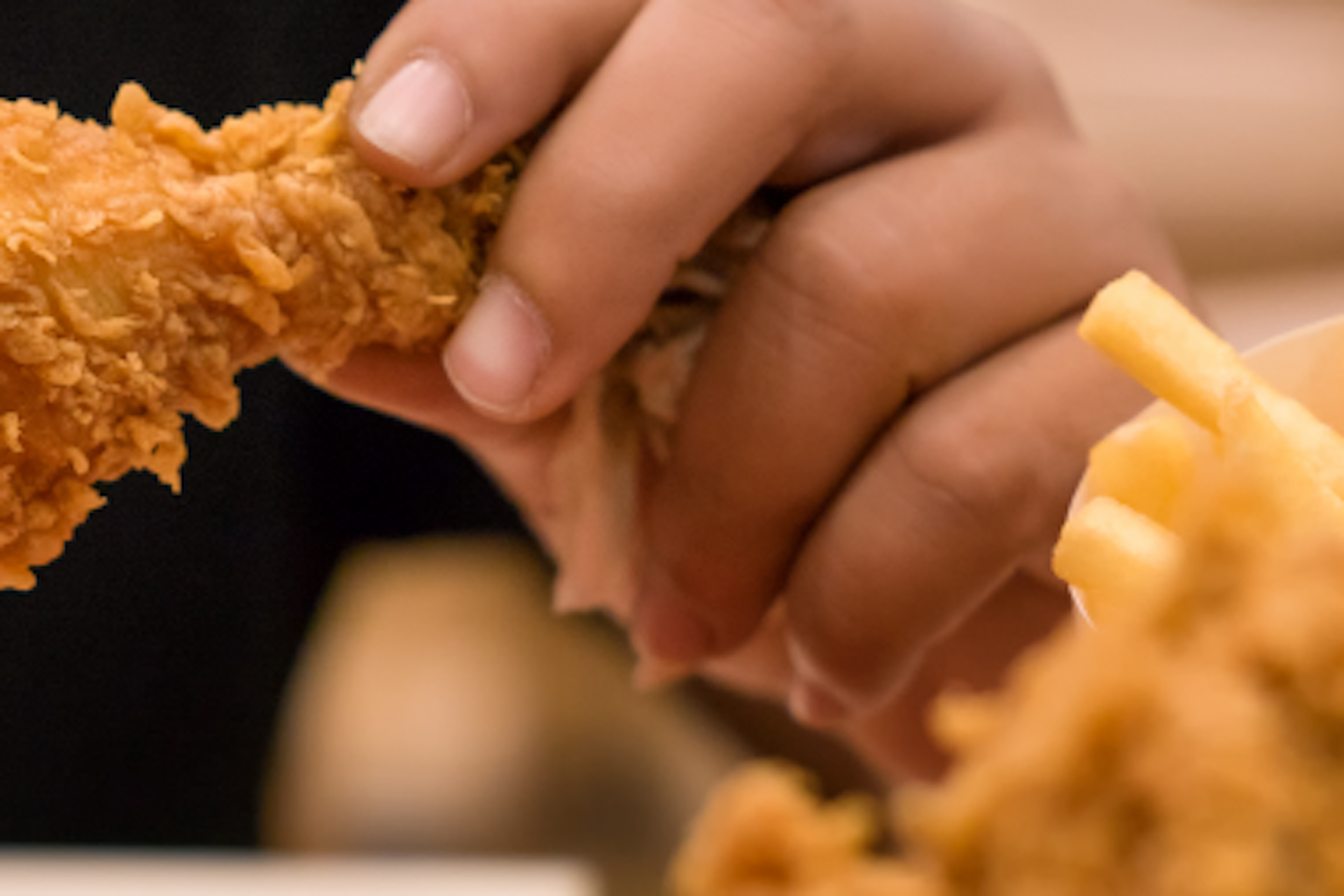 Hand holding a fried chicken drumstick with a black background. 