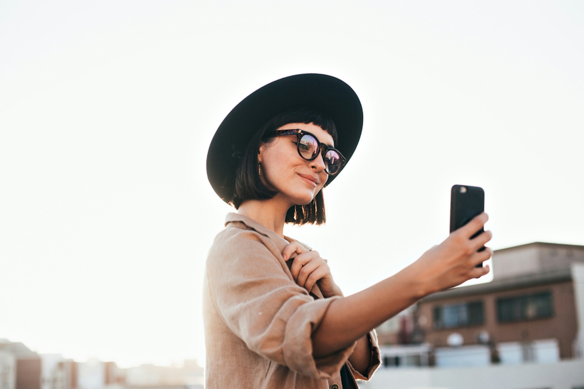 A woman in a wide-brimmed hat taking a selfie on her smartphone