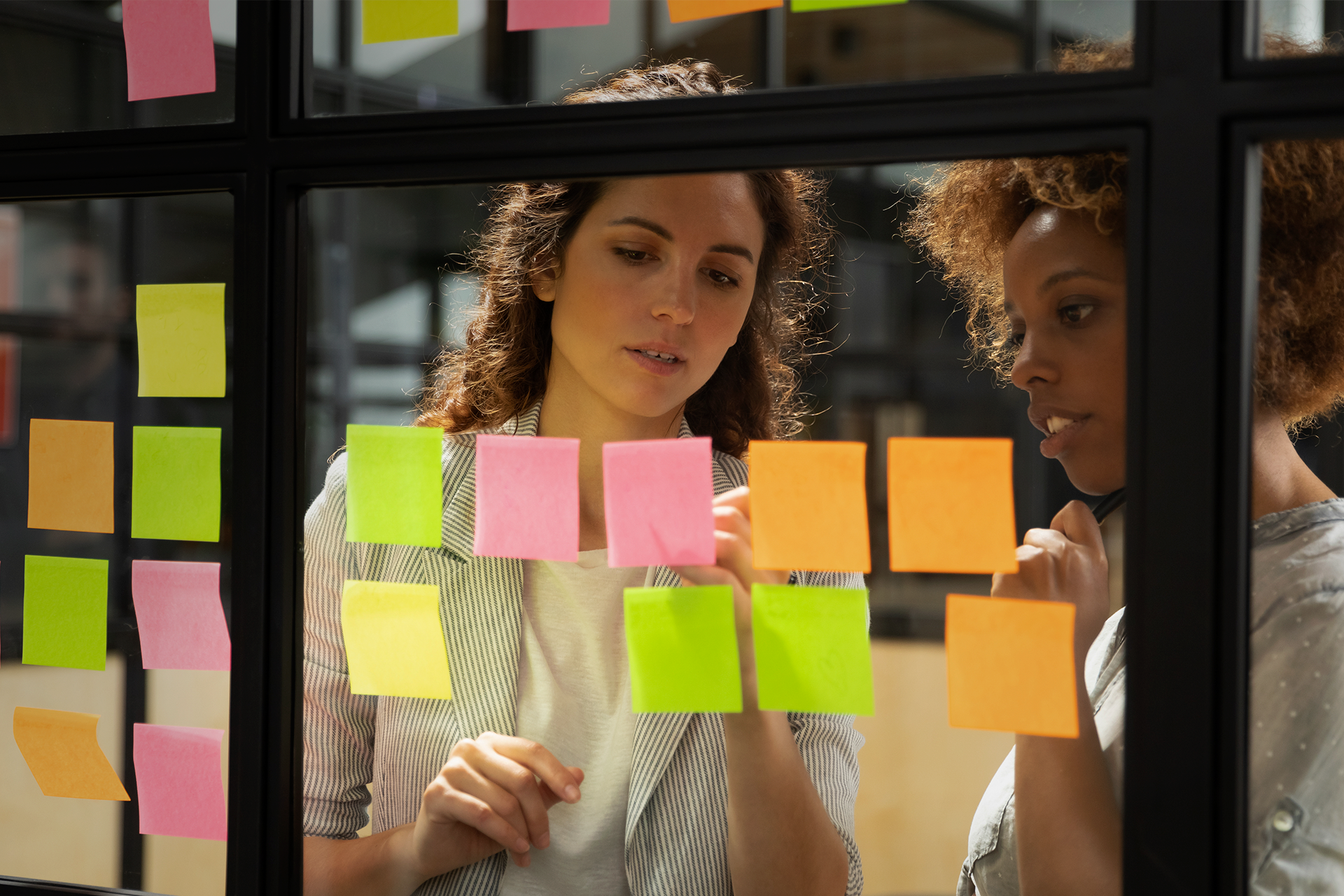 Two young professional women in an office looking at multi-colored sticky notes