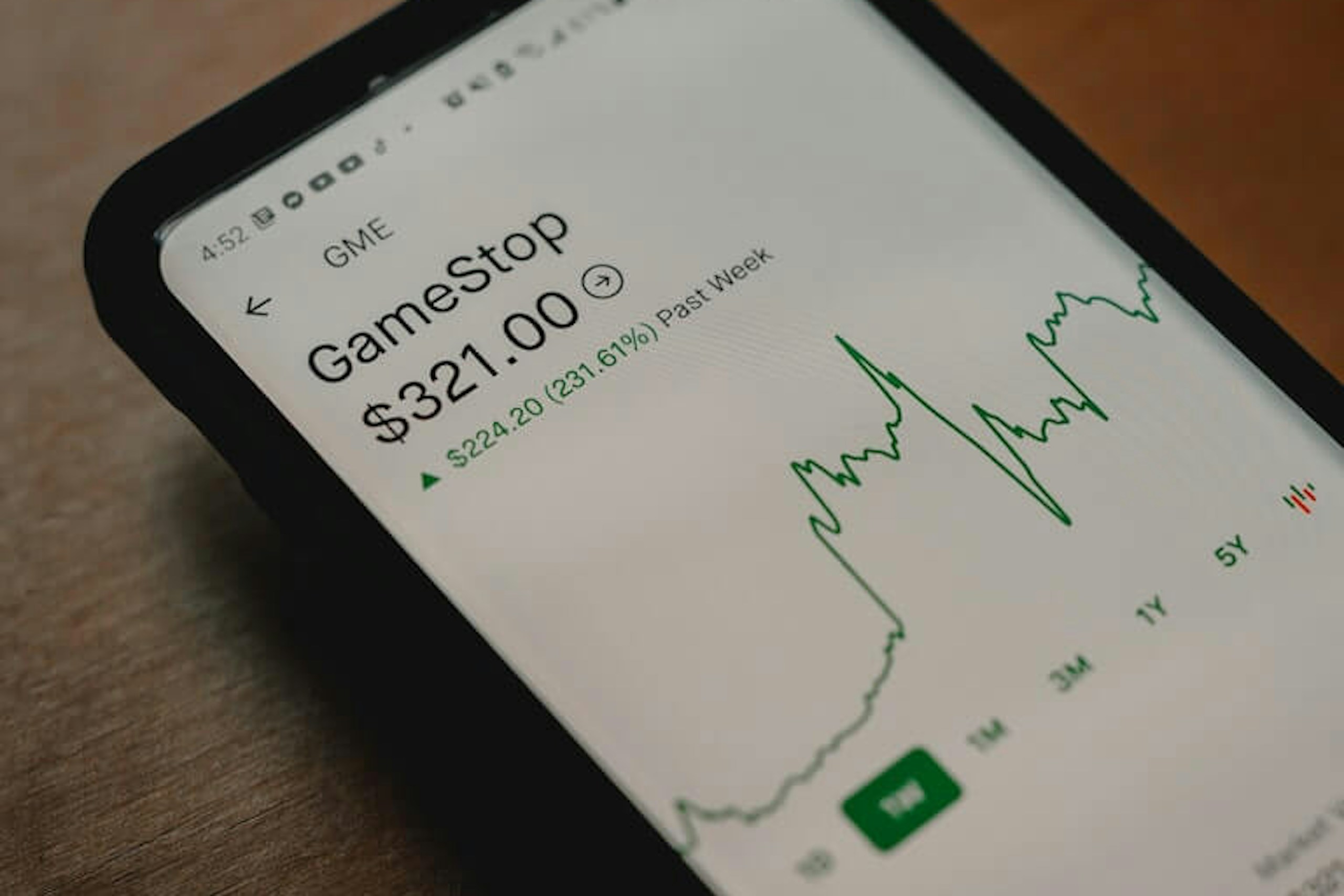 Man sieht ein Smartphone auf einem Holztisch liegen, auf dem gerade der GME GameStop Aktienkurs abgerufen wird.