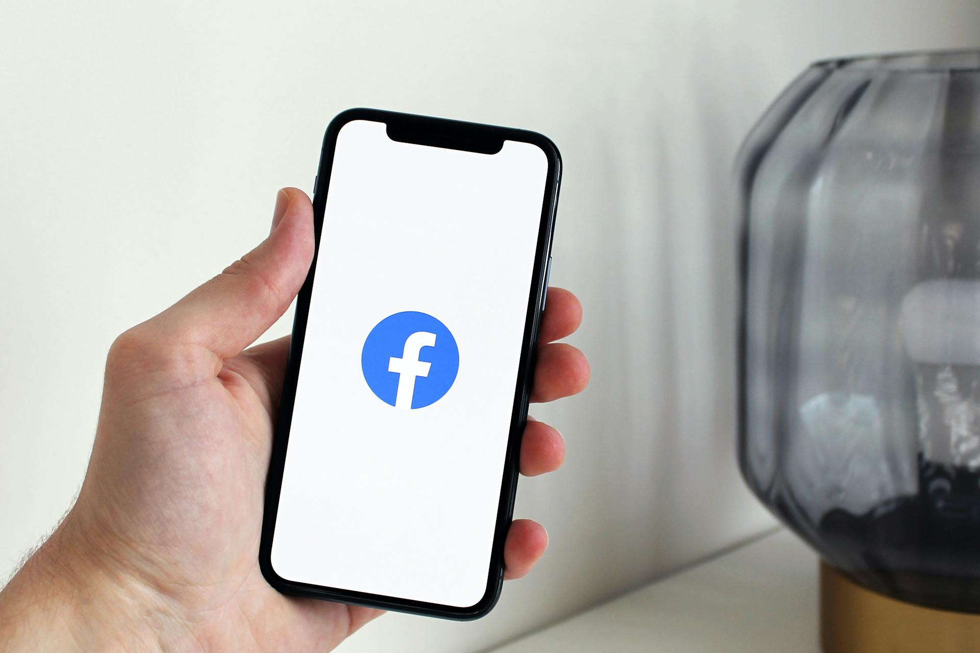 Een hand houdt een smartphone vast die het Facebook logo afbeeldt