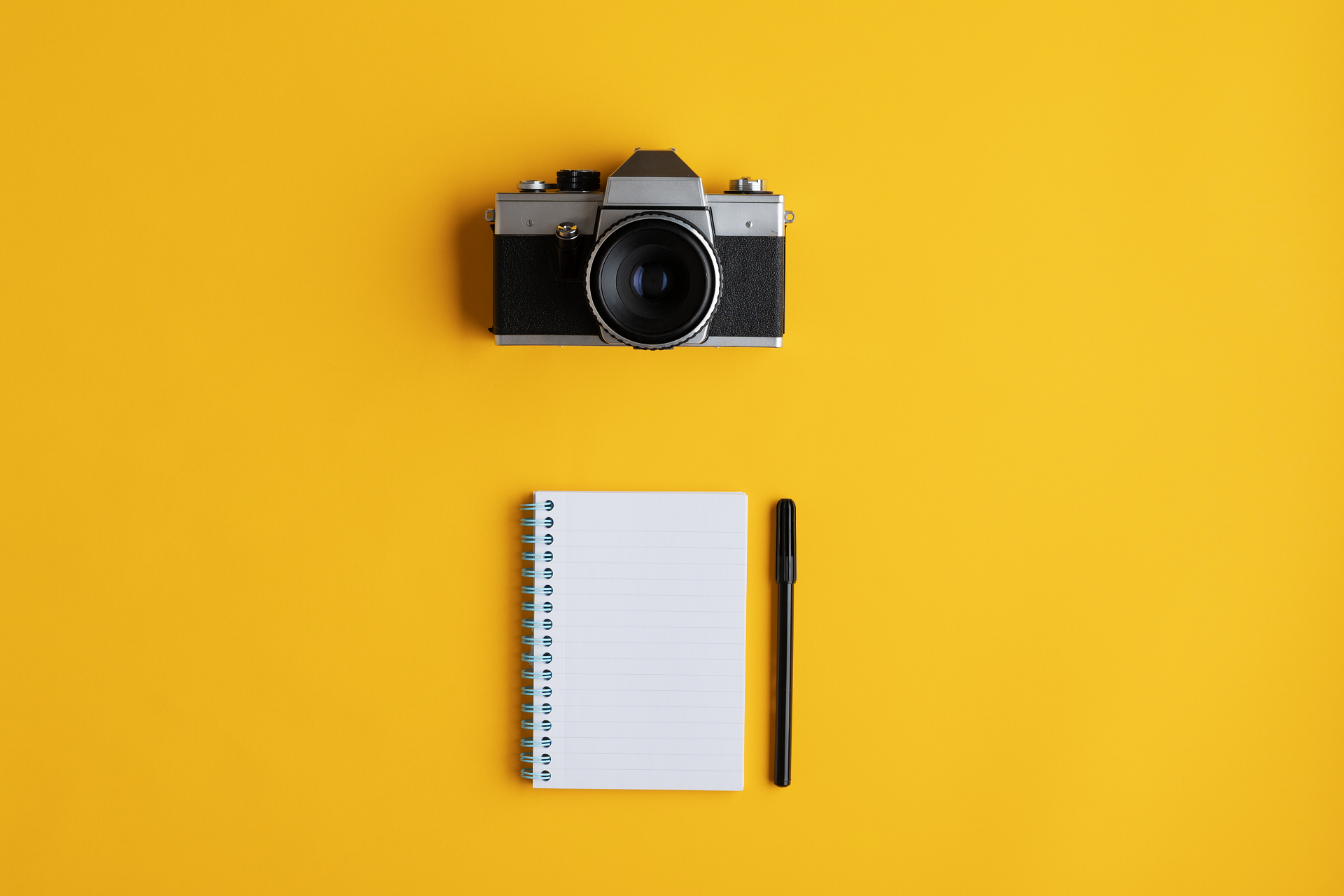 An image of a camera and a notepad on yellow background.