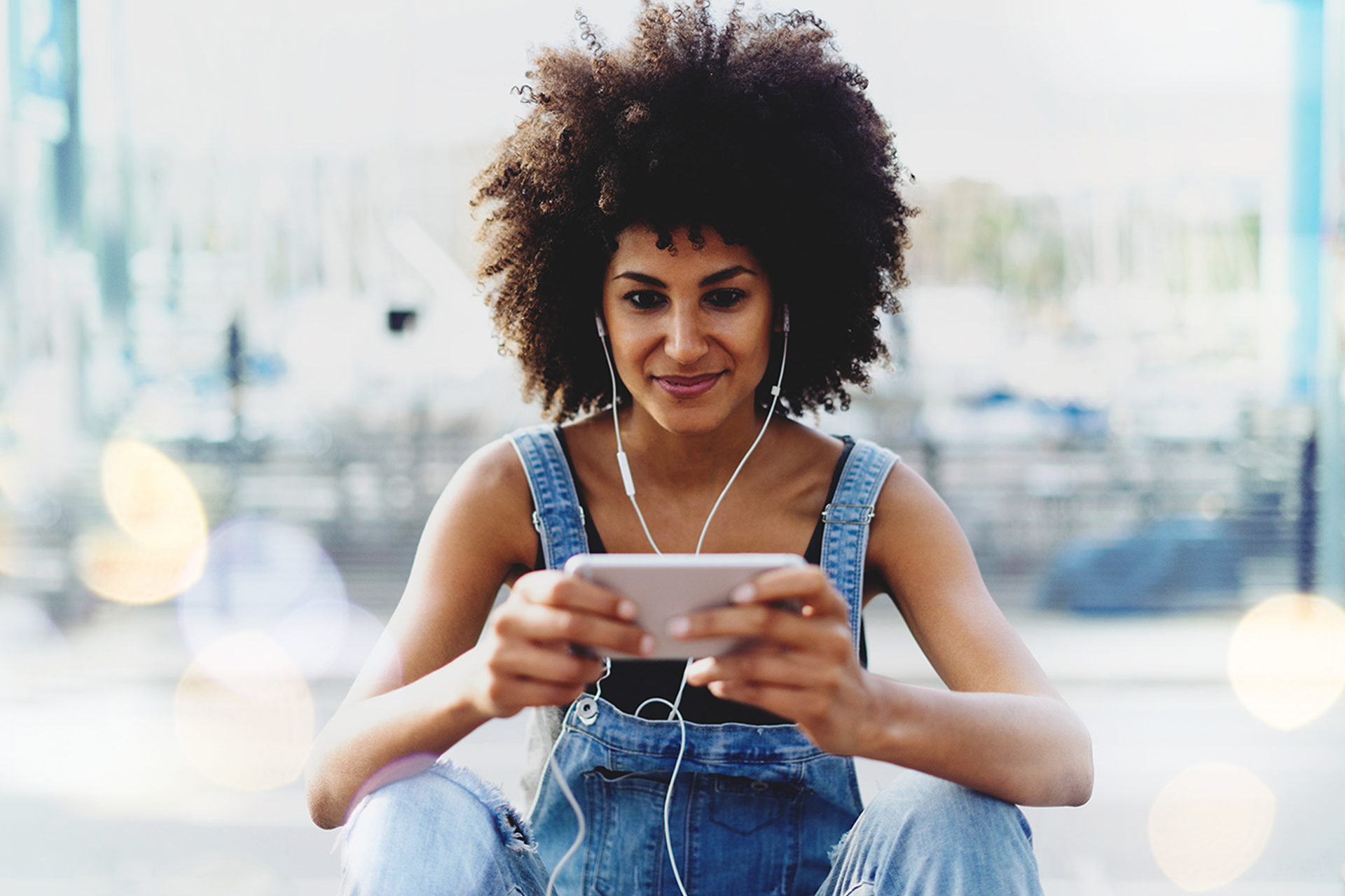 Woman wearing dungarees watching a video on her phone with earphones