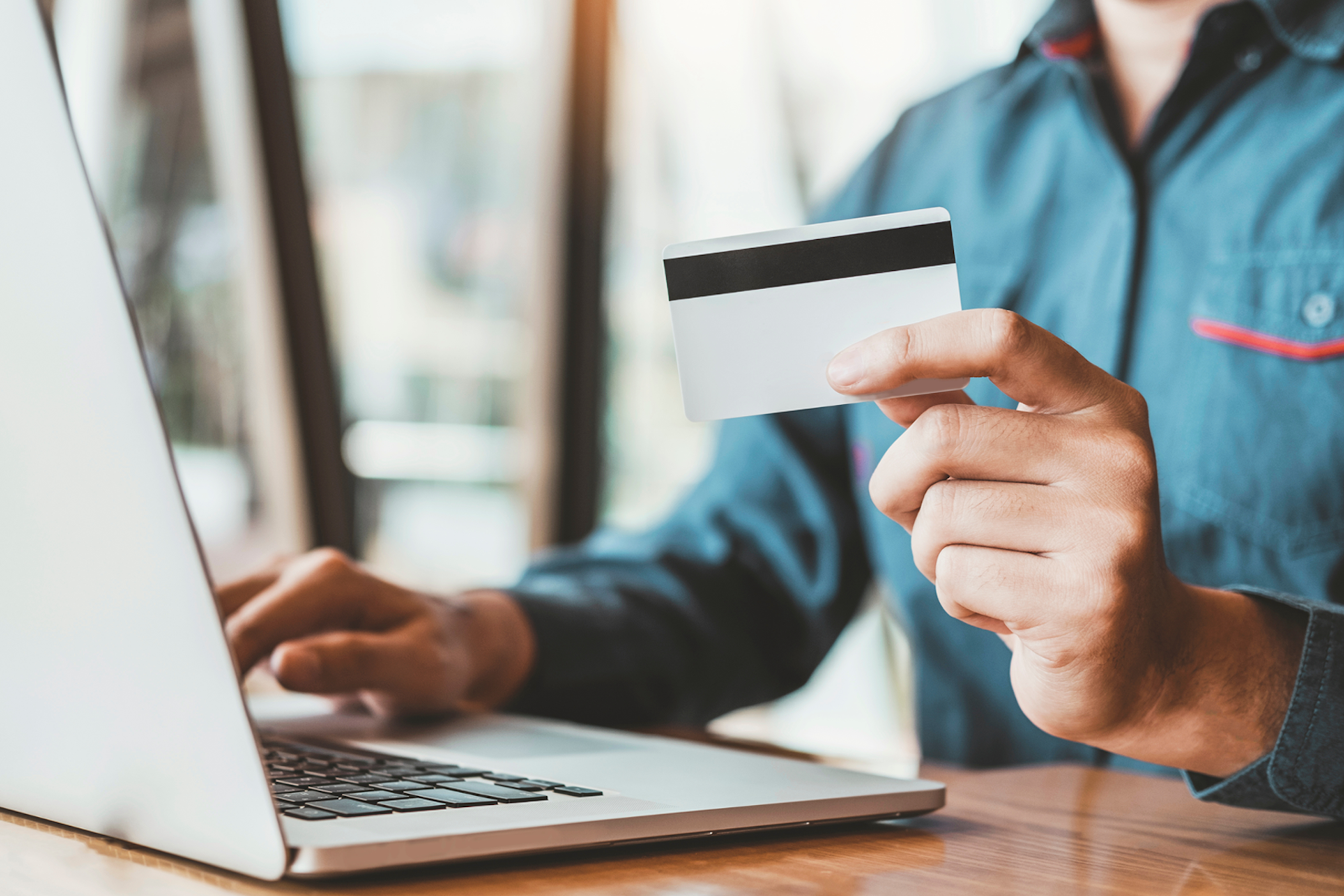 A person types at a laptop and holds a credit card in this image for Meltwater's Industry Snapshot: Banking and Financial Services