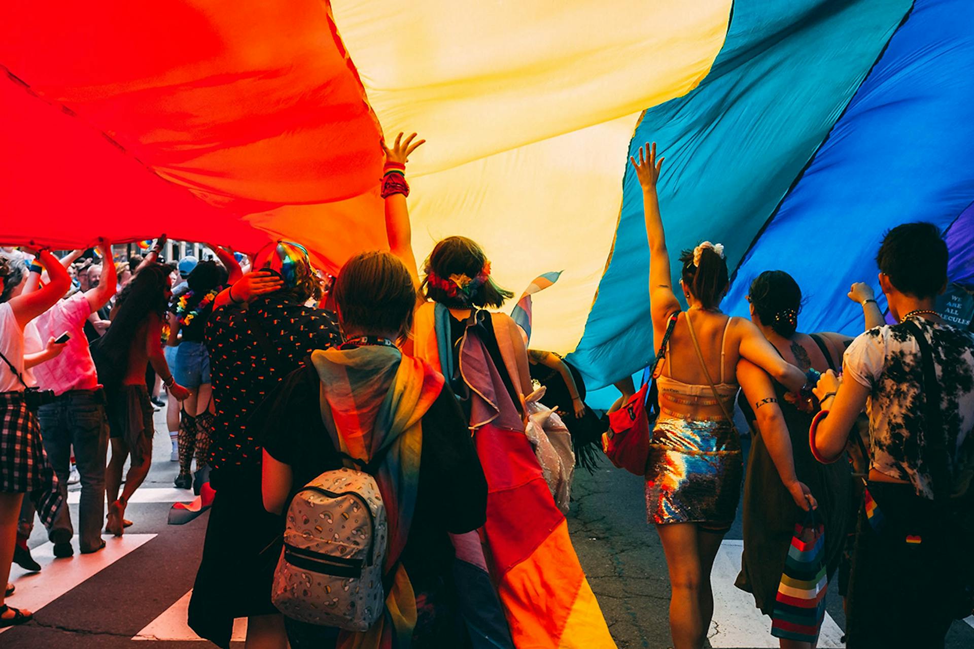 People stand underneath a giant rainbow flag in this image for a blog about five things brands should remember during Pride Month.